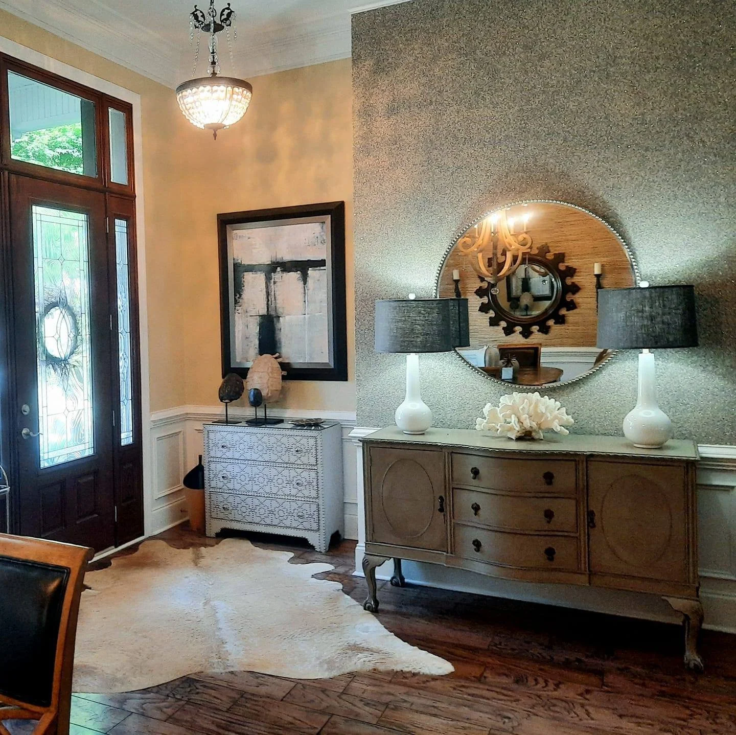 Entryway with a sunburst mirror, gray console table, and cowhide rug designed by Bonnie Boyette Designs