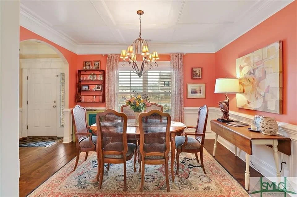 Dining room with coral walls, a brass chandelier, wood dining table, and Oriental rug designed by Bonnie Boyette Designs