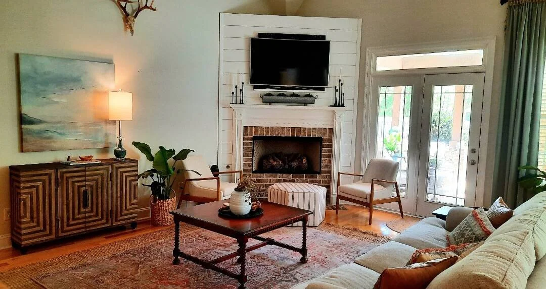 Living room with a white brick fireplace, landscape painting, wood coffee table, and French doors designed by Bonnie Boyette Designs