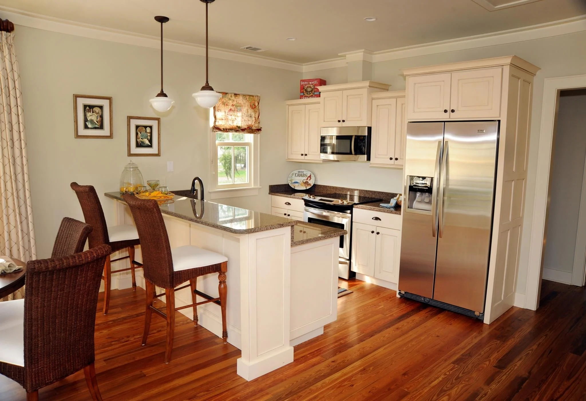 White kitchen with a large island, pendant lights, and hardwood floors designed by Bonnie Boyette Designs