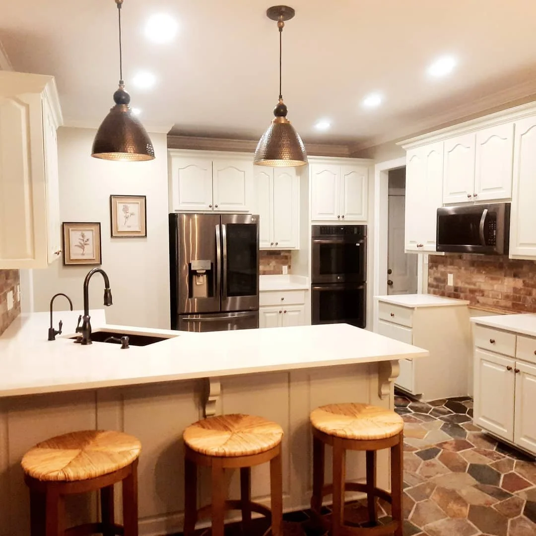 Kitchen with white shaker cabinets, black pendant lights, and a breakfast bar with wood stools designed by Bonnie Boyette Designs