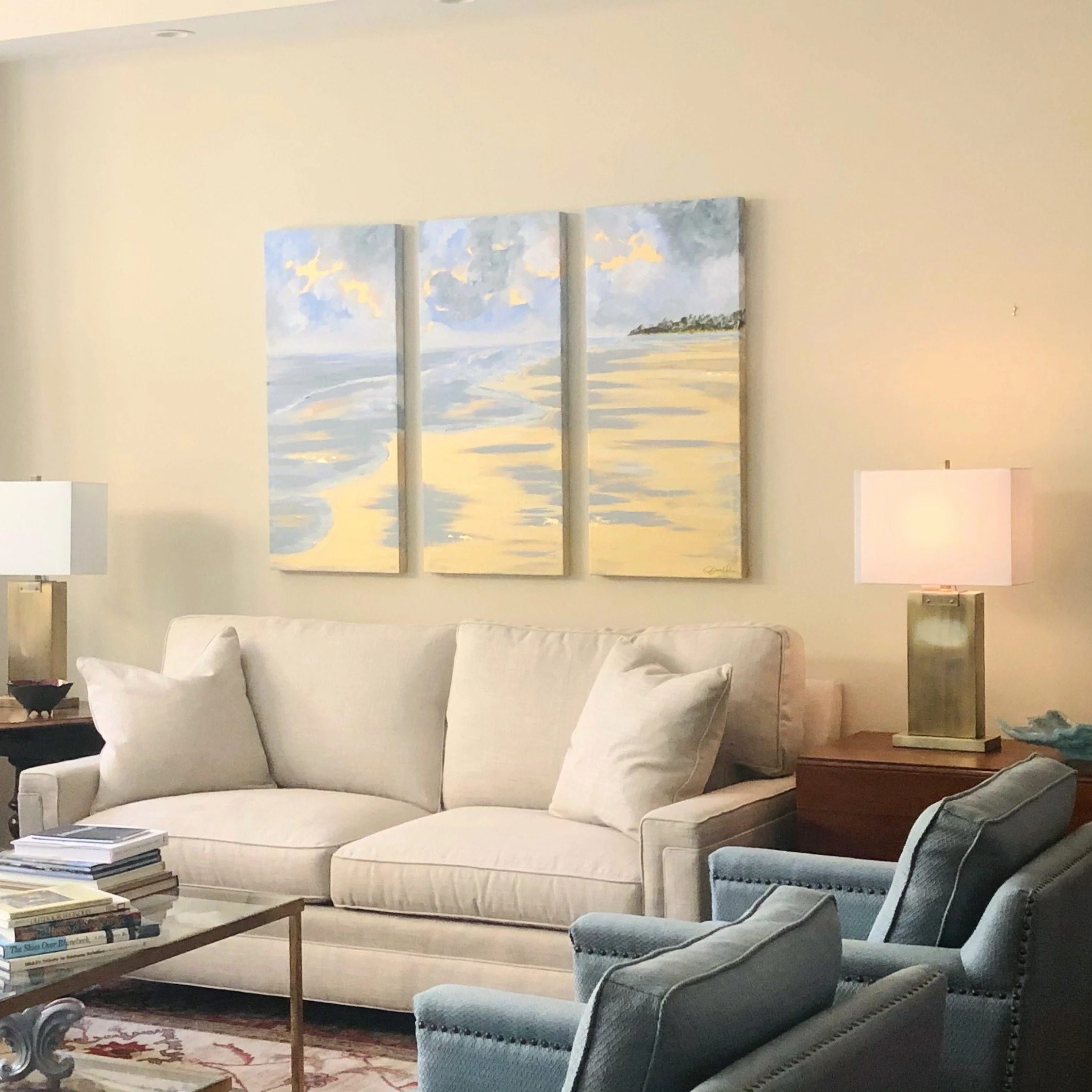 Living room with a cream sofa, blue accent chairs, table lamps, and large abstract artwork designed by Bonnie Boyette Designs