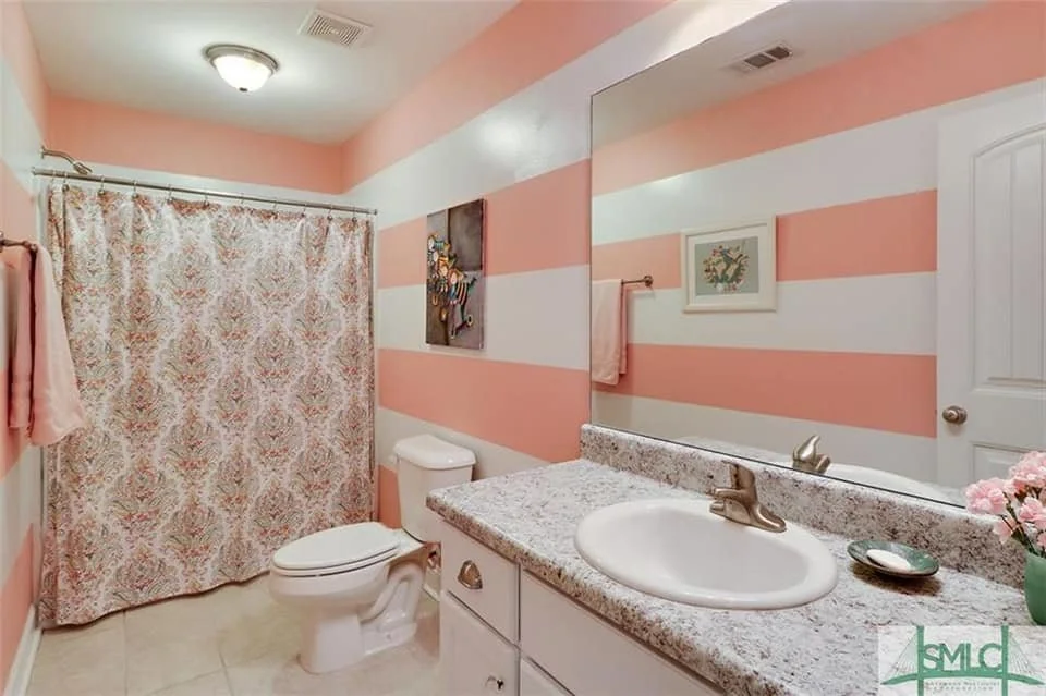 Bathroom with pink and white striped walls, floral shower curtain, and granite vanity designed by Bonnie Boyette Designs