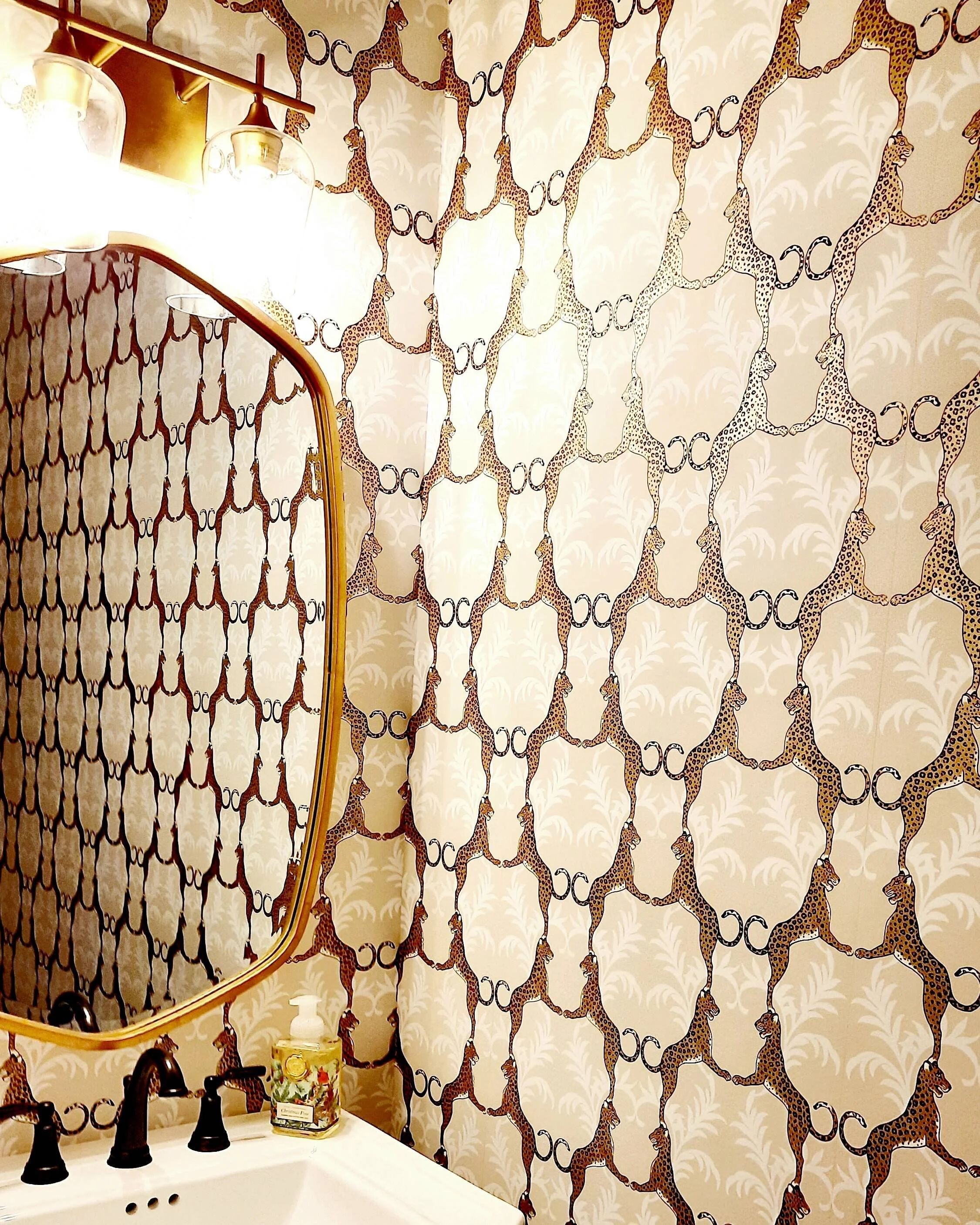 Powder room with bold black and cream patterned wallpaper and a round gold mirror designed by Bonnie Boyette Designs