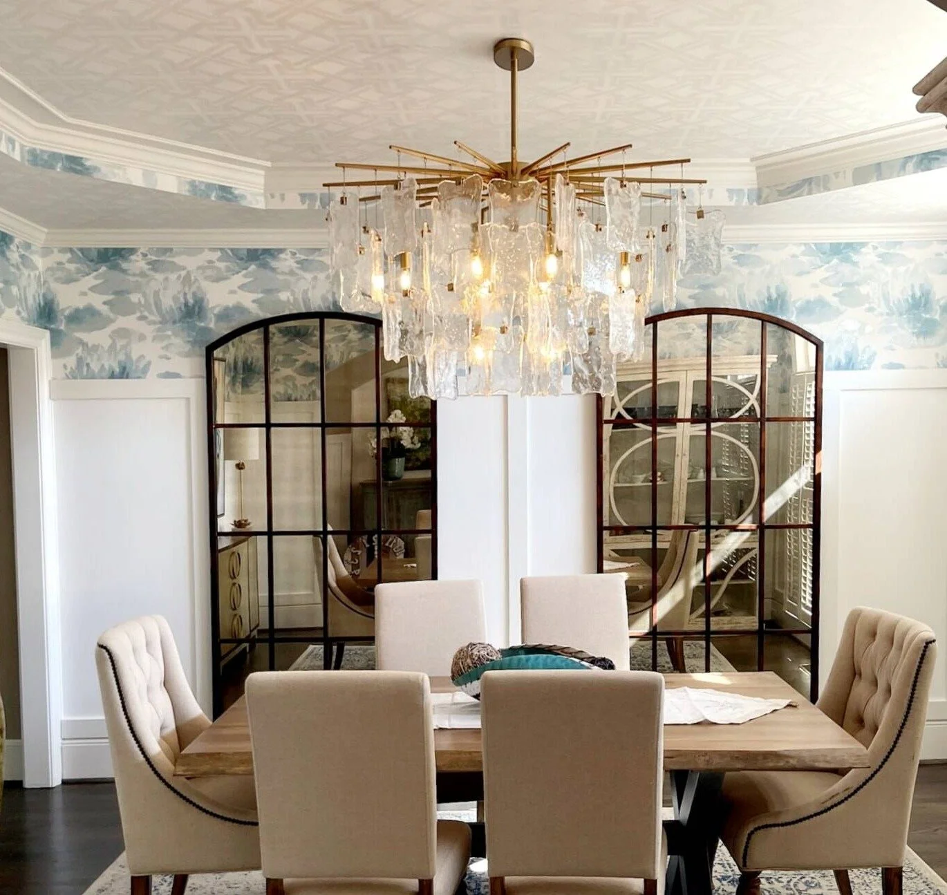 Dining room with a glass chandelier, arched black mirrors, and blue toile wallpaper designed by Bonnie Boyette Designs