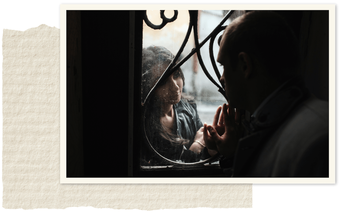 A woman and a man on opposite sides of a window, touching hands through the glass in a close, intimate moment.