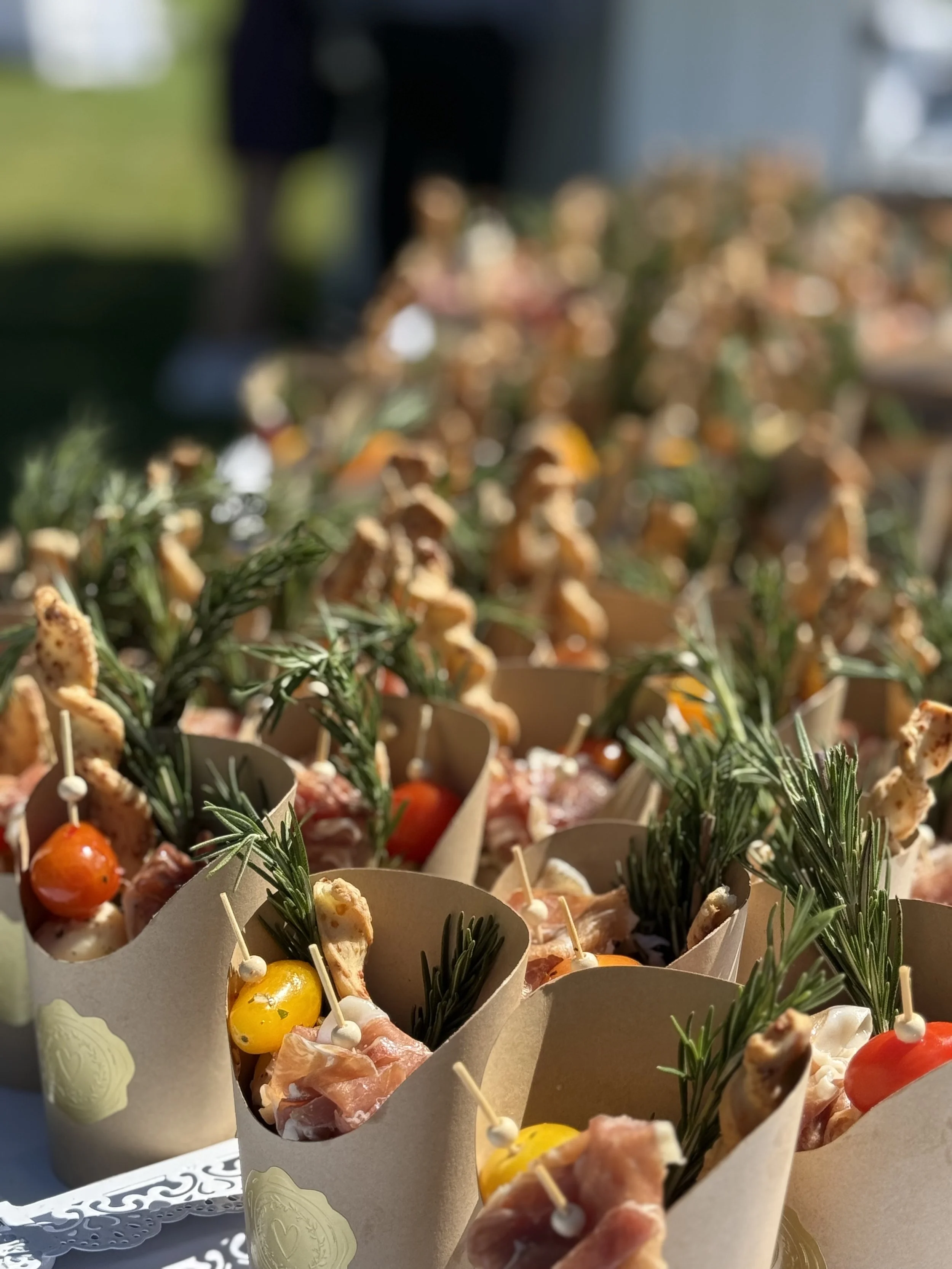 Small appetizers with cherry tomatoes, herbs, and skewered meats in paper wrappers.