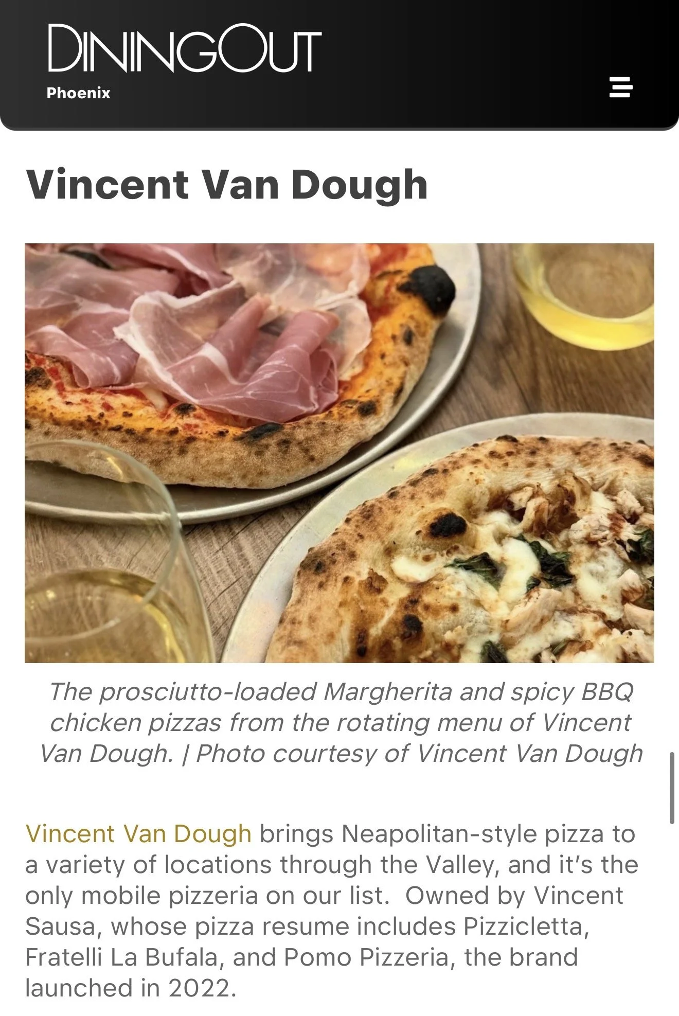 Close-up of two Neapolitan-style pizzas, one topped with prosciutto, and the other with cheese, tomato, and basil, with glasses of white wine on a wooden table.