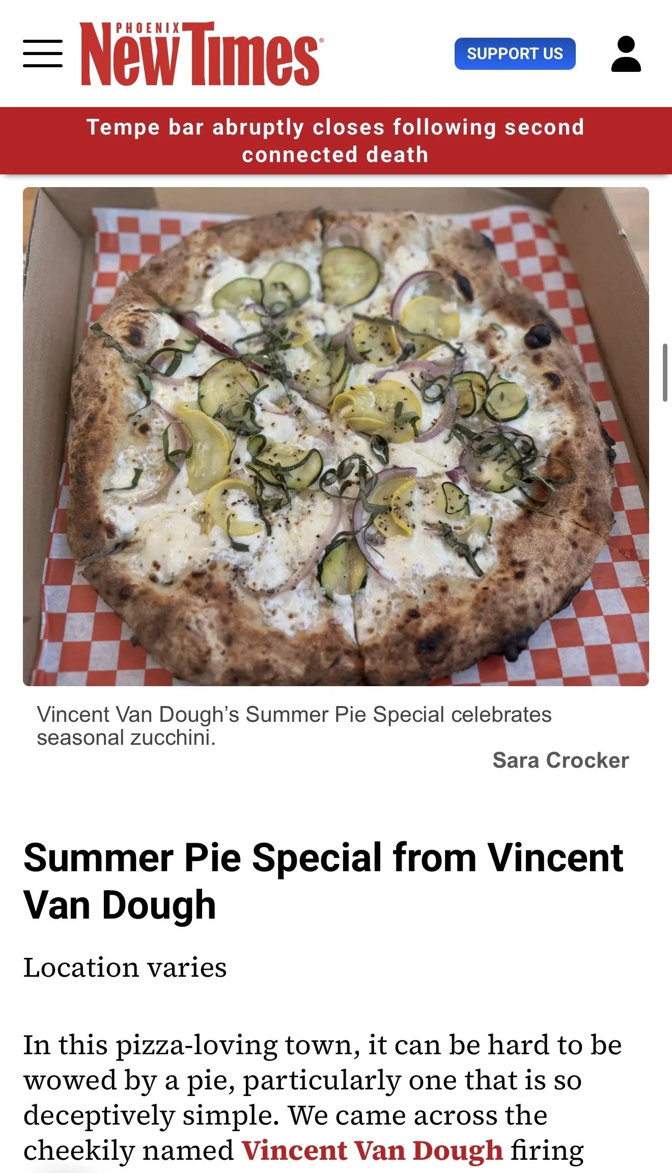 A pizza with zucchini, onions, and herbs in a pizza box lined with red and white checkered paper.