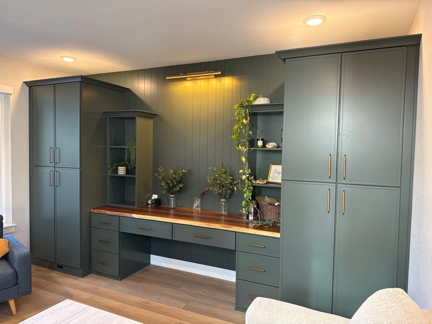 Interior view of a built-in green cabinet with open shelving, a wooden countertop, and decorative plants.