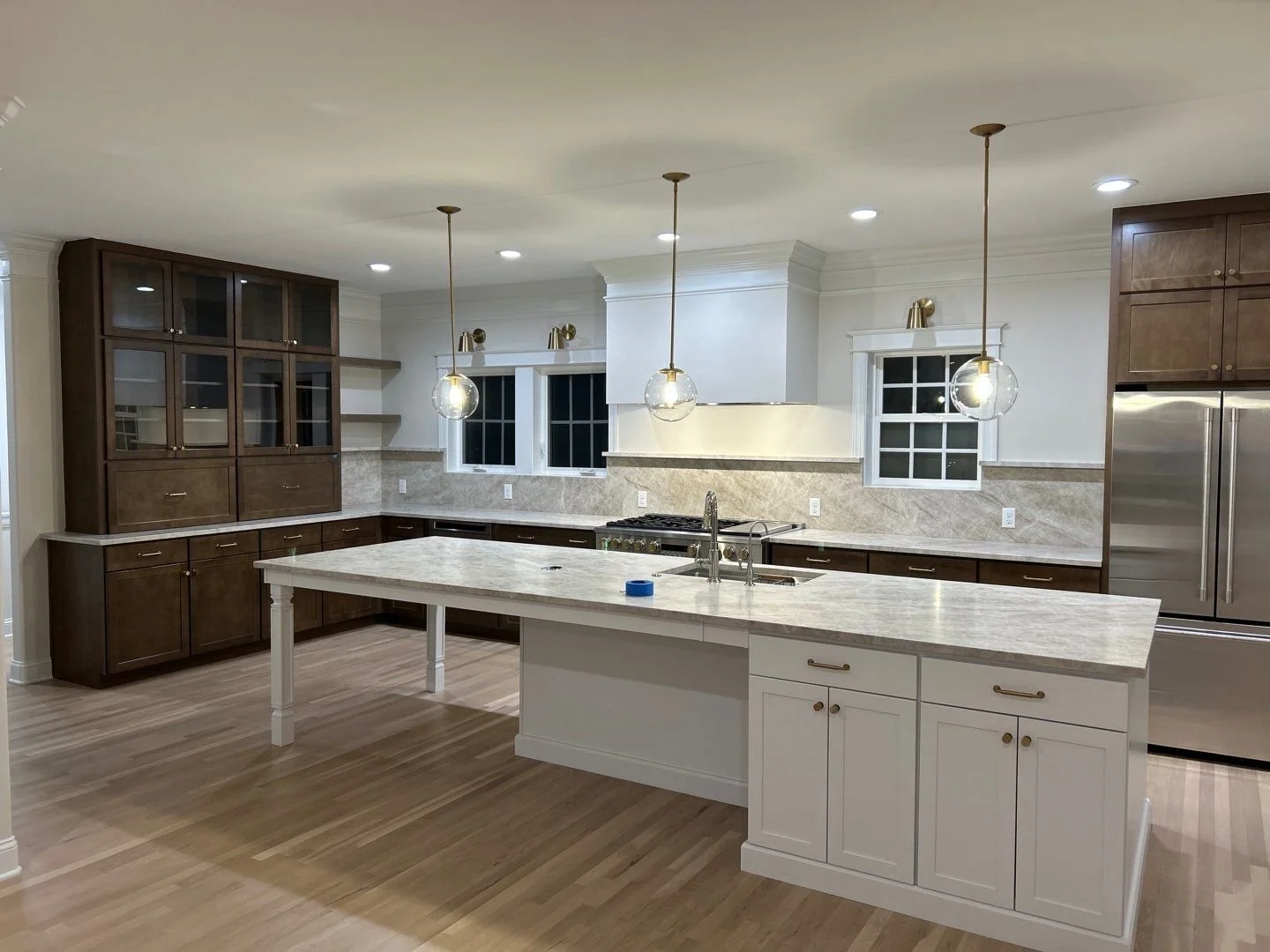 Modern kitchen with white island, dark wood cabinets, stainless steel refrigerator, and three pendant lights.