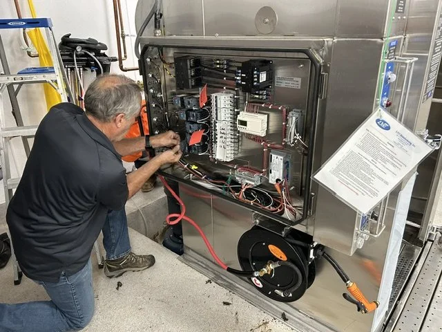 Technician working on an industrial electrical control panel with exposed wiring and components.