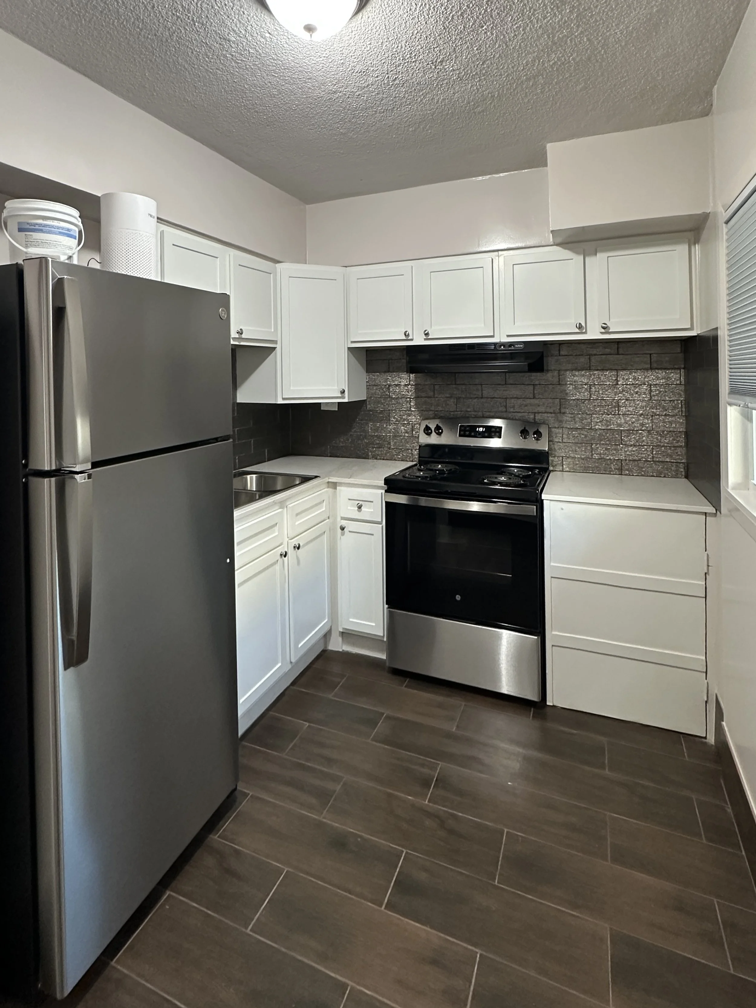 A kitchen with white cabinets, a stainless steel refrigerator, a black and stainless oven, gray tile backsplash, and brown flooring.