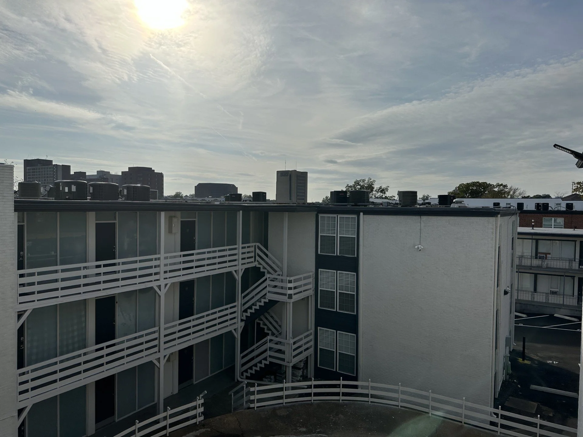 View of a city skyline with modern buildings, ventilation units, and a partly cloudy sky with the sun shining.
