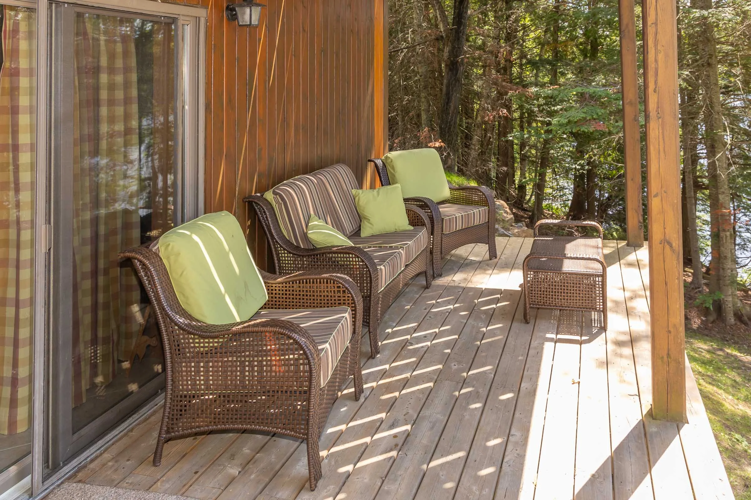 A wooden deck with outdoor furniture including a sofa and chairs with green and striped cushions, surrounded by trees and nature.