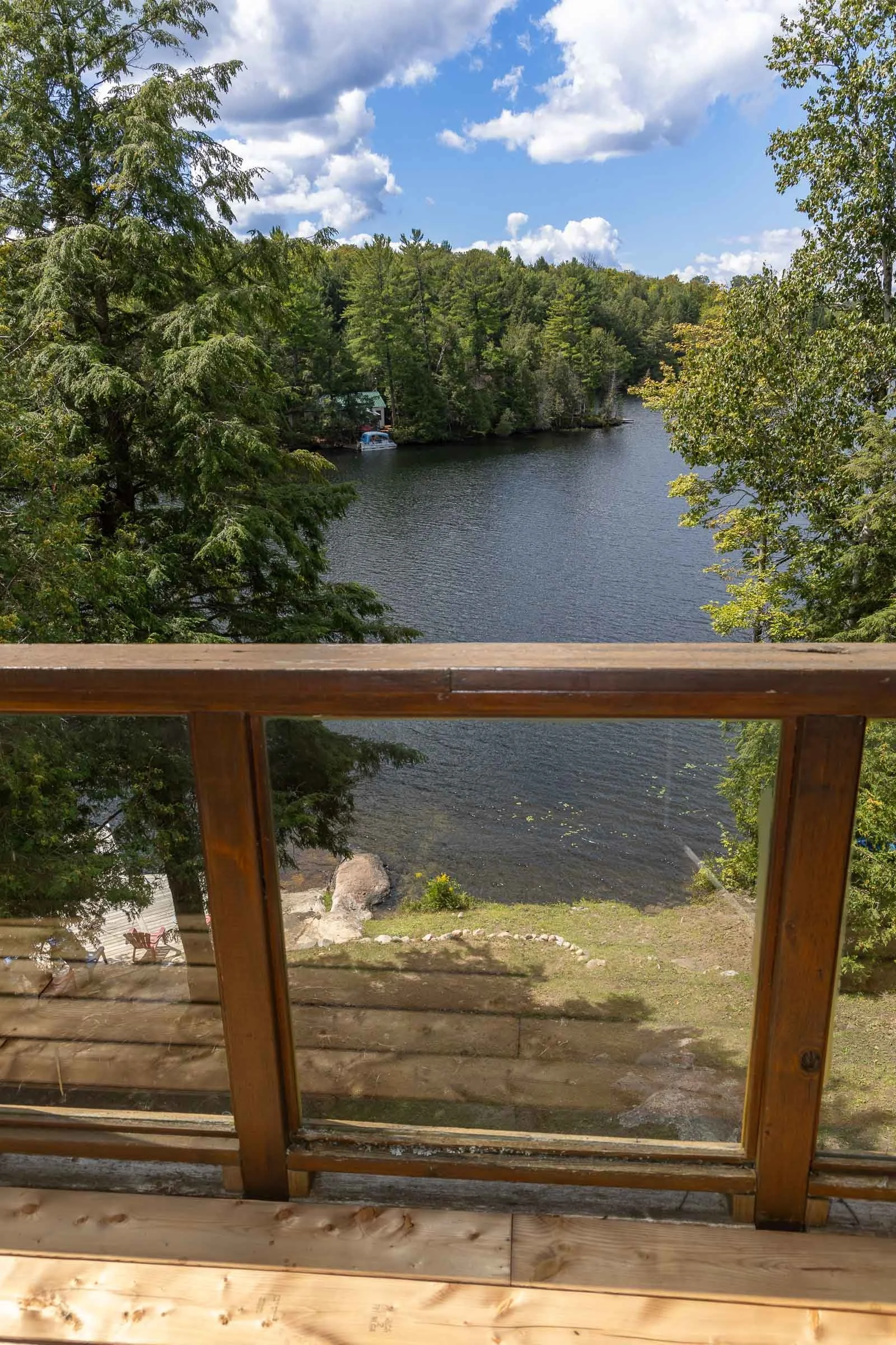Scenic view of a lake surrounded by trees with a partly cloudy sky, seen through a wooden window frame.