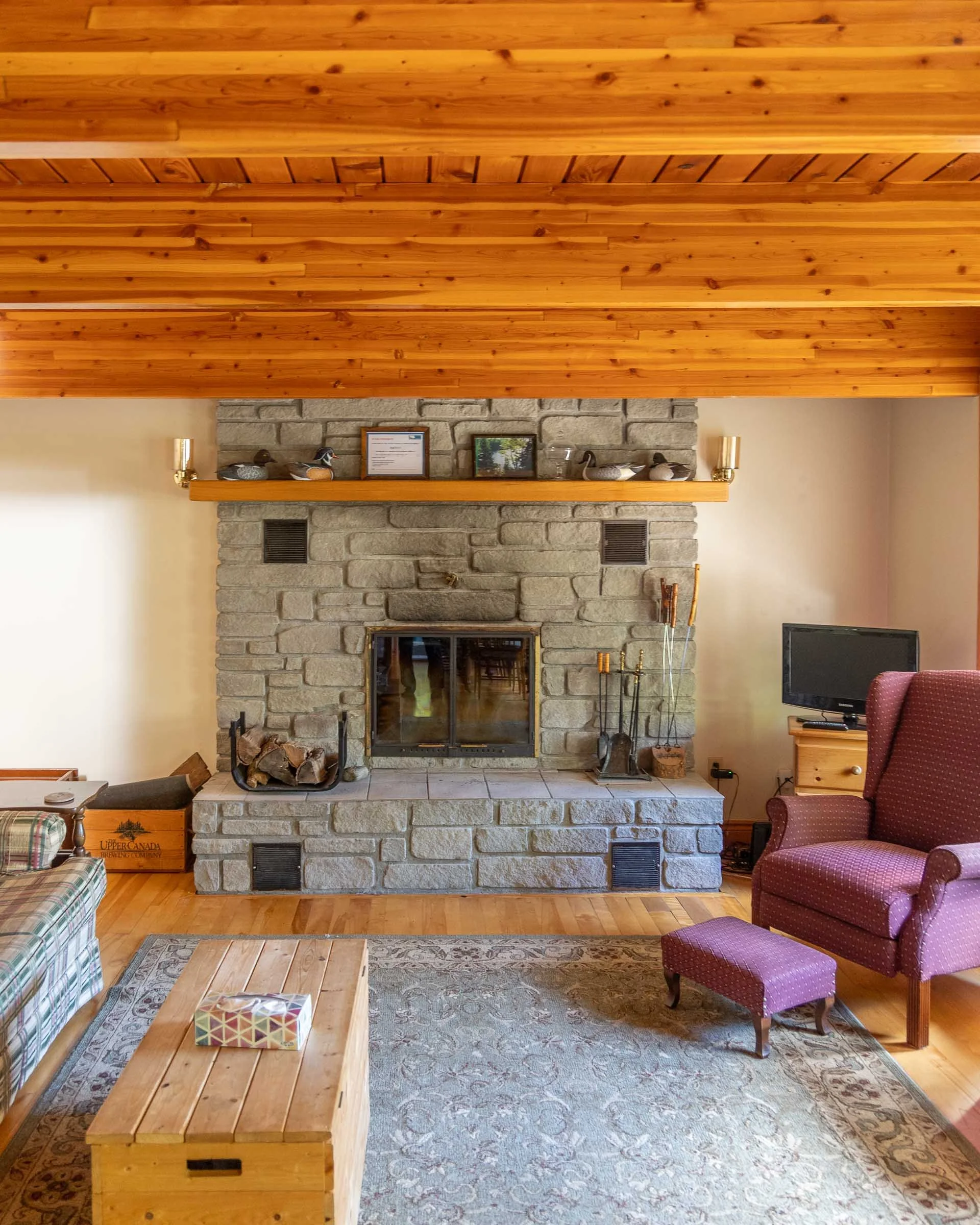 Living room with a large stone fireplace, wooden ceiling, and various chairs and furniture.