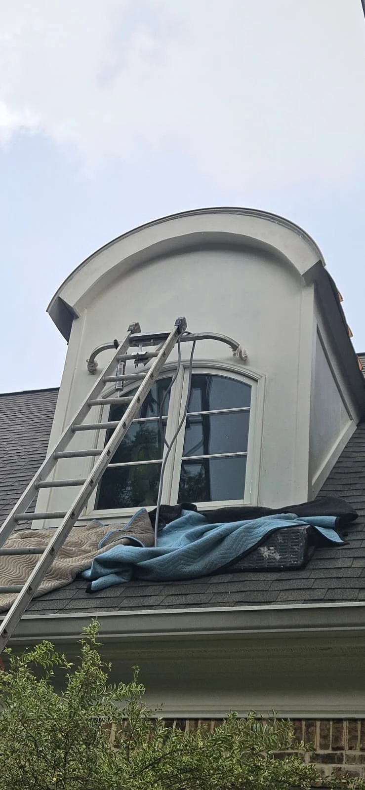 Ladder leaning against an arched window on a house with a tarp and blanket on the roof below.
