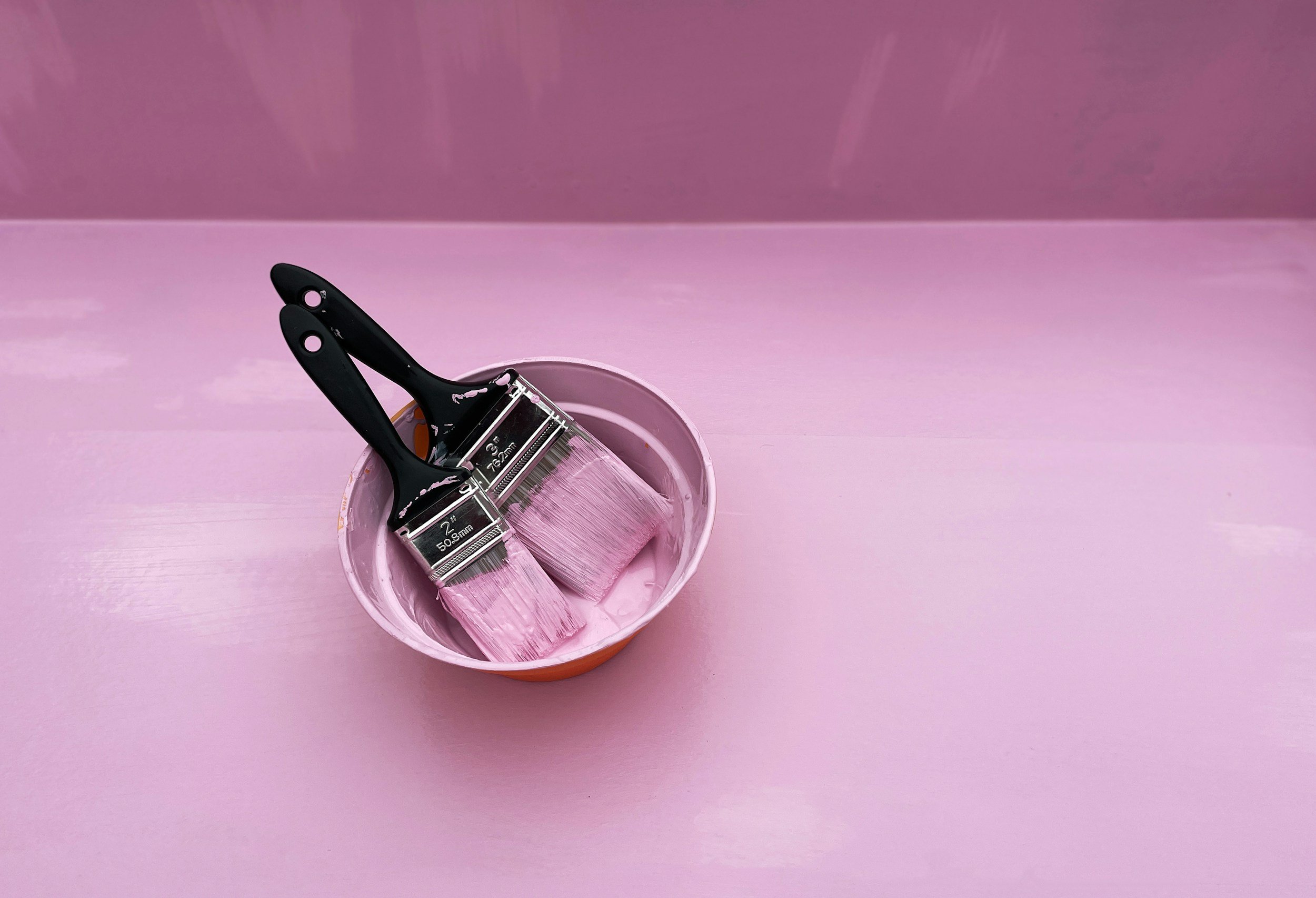 Paintbrushes with pink paint in a pink container on a pink surface.