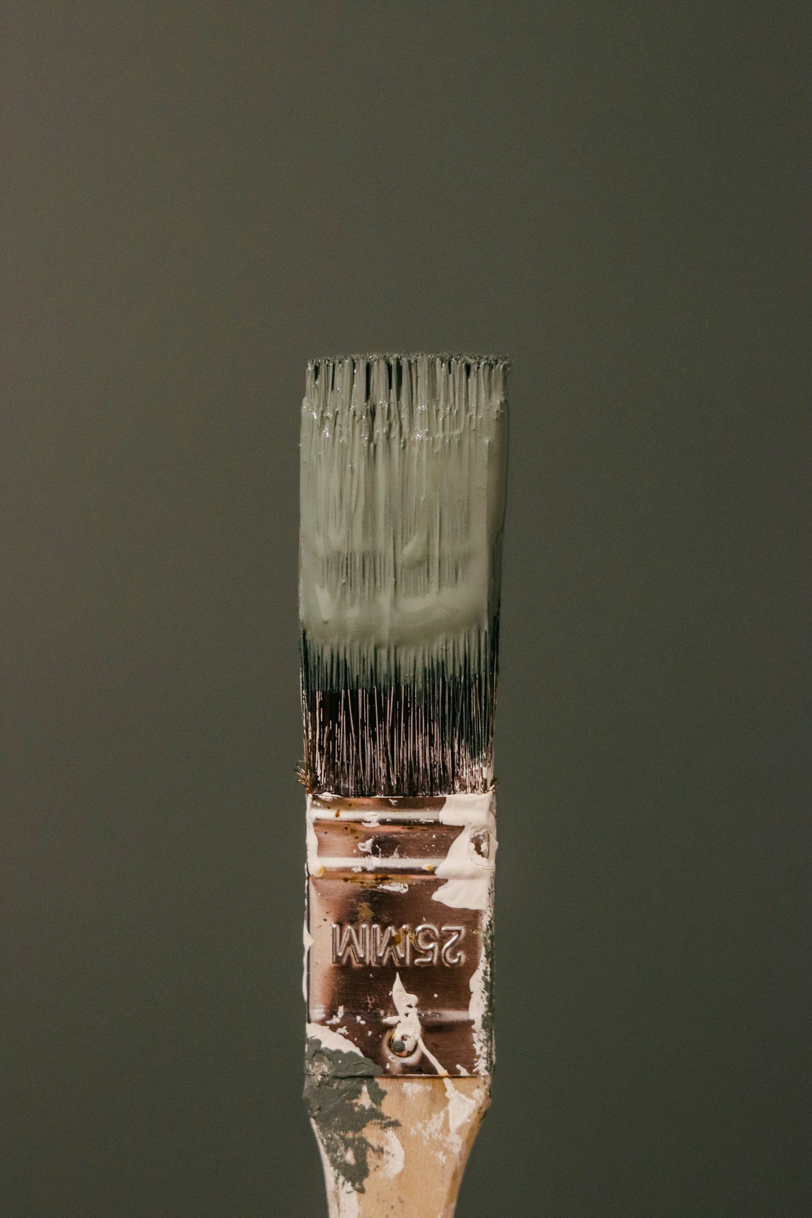 Close-up of a paintbrush with white paint and peeling bristles against a gray background.