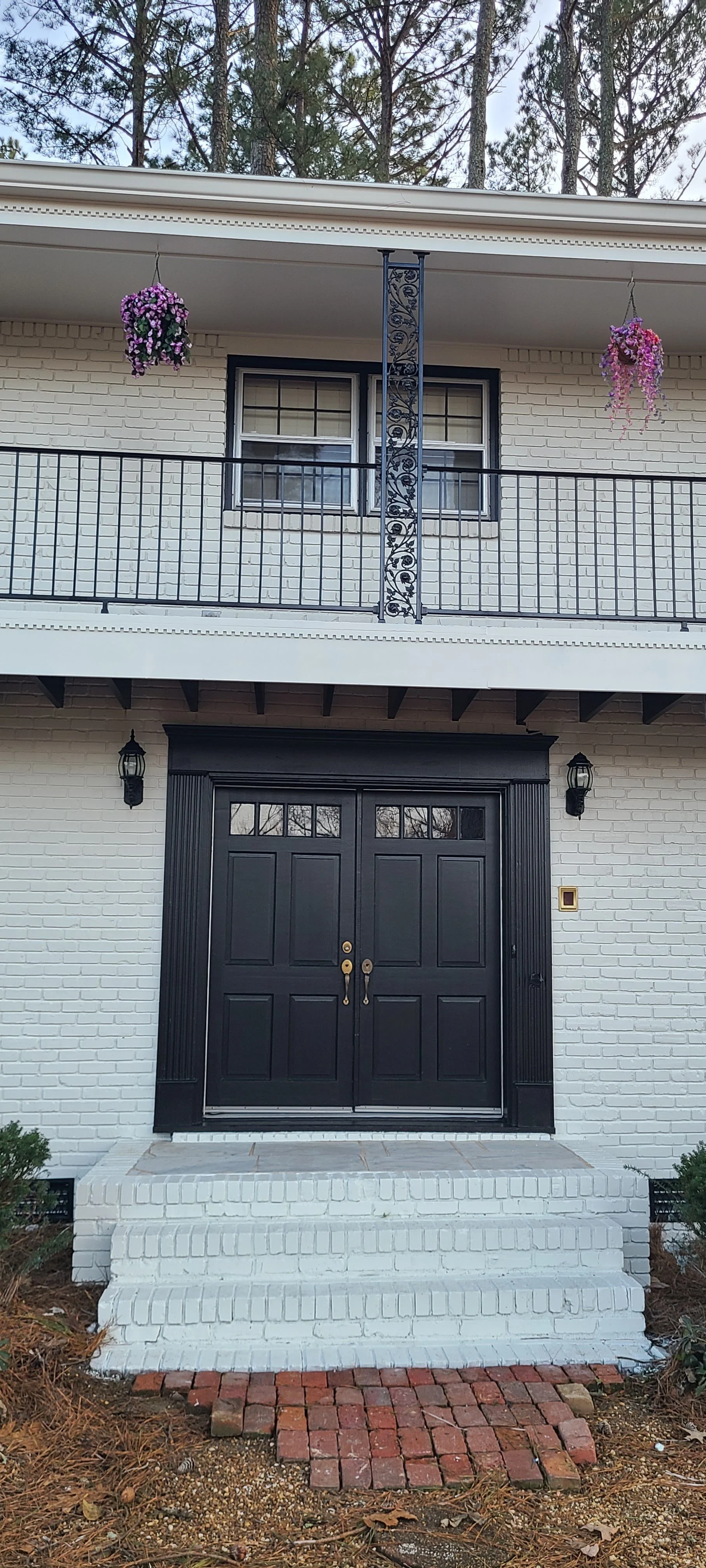 Front view of a house with black double doors, white brick exterior, steps, and a brick-paved pathway.