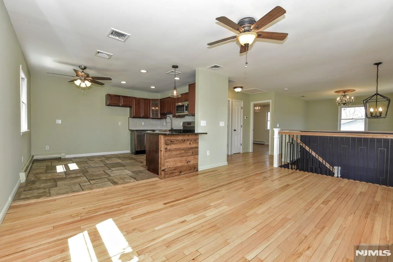 Open-concept living area with hardwood floors, kitchen with dark wood cabinets, and multiple ceiling fans and light fixtures.