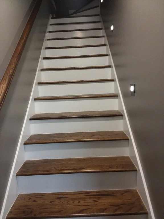 Interior staircase with wooden steps and gray walls, illuminated by small wall lights.