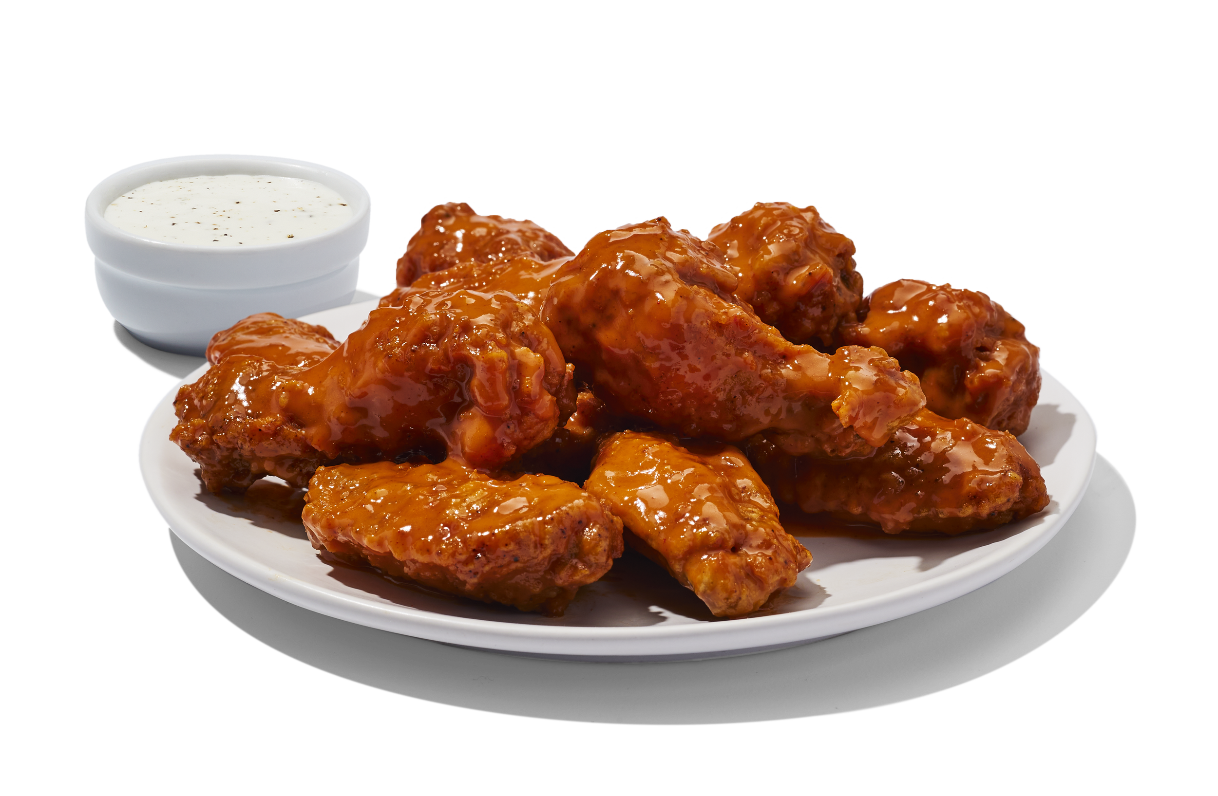 Plate of glazed chicken wings with a side of creamy dipping sauce.