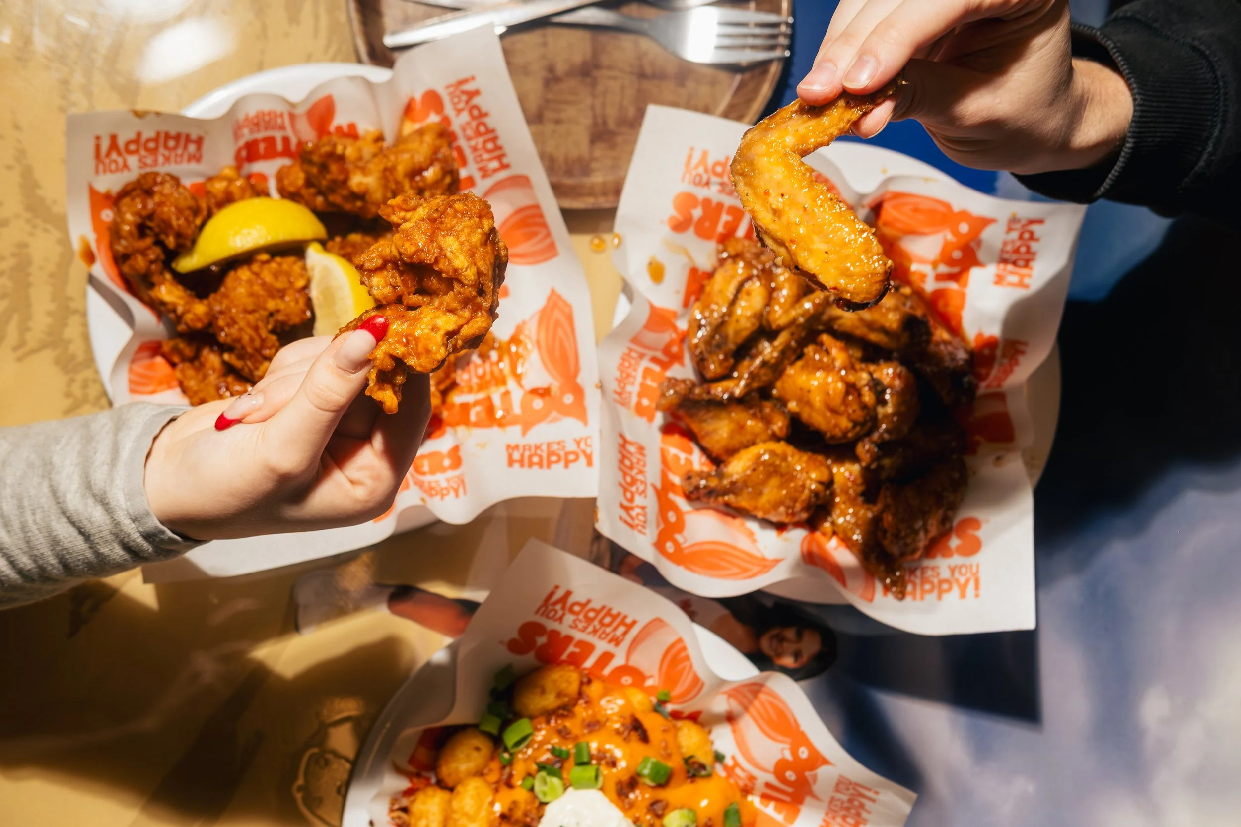 People enjoying fried chicken wings and other snacks at a table, with Lindsey's Happy menu paper liners.