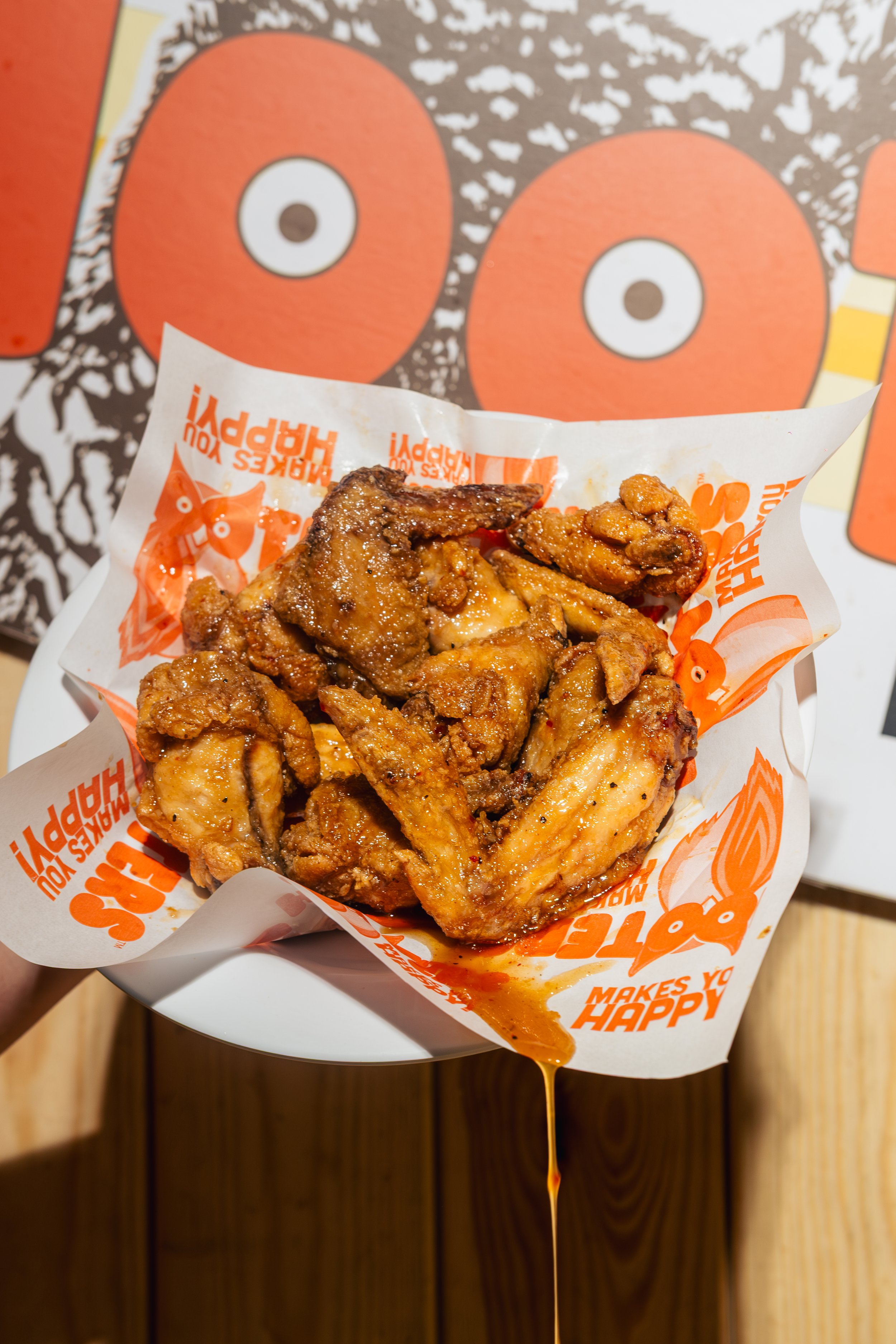 Close-up of fried chicken in a basket with sauce, with a colorful cartoon character poster in the background.