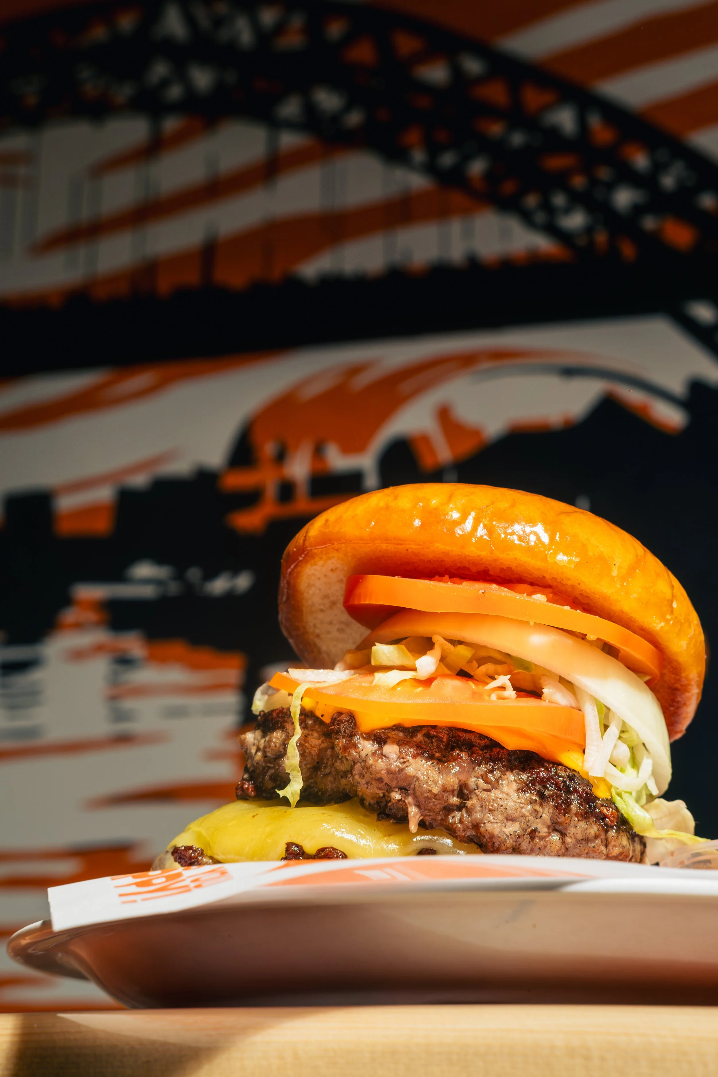 Close-up of a cheeseburger with toppings including lettuce, tomato, cheese, and a grilled beef patty on a bun, on a plate with a blurry background.