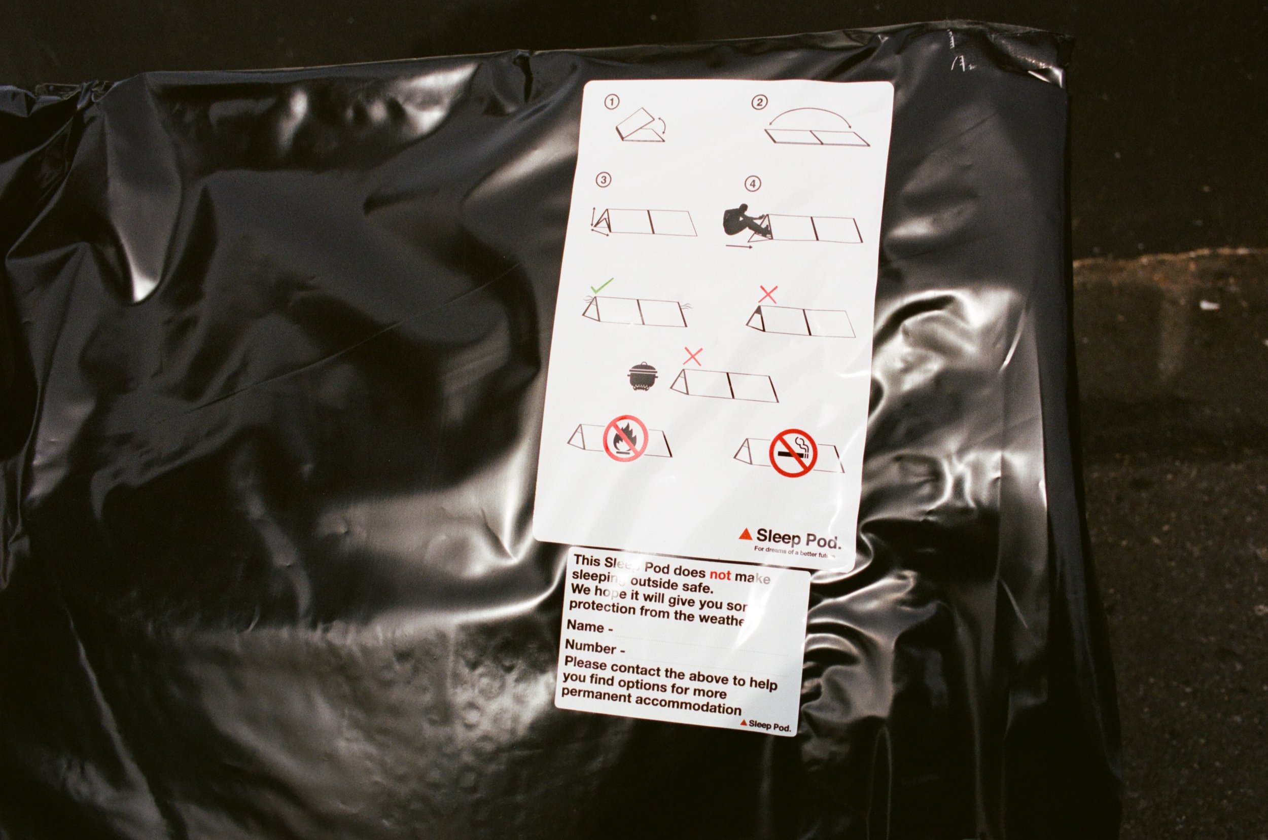 A black sleep pod package with assembly instructions and safety warnings attached, lying on a dark surface.