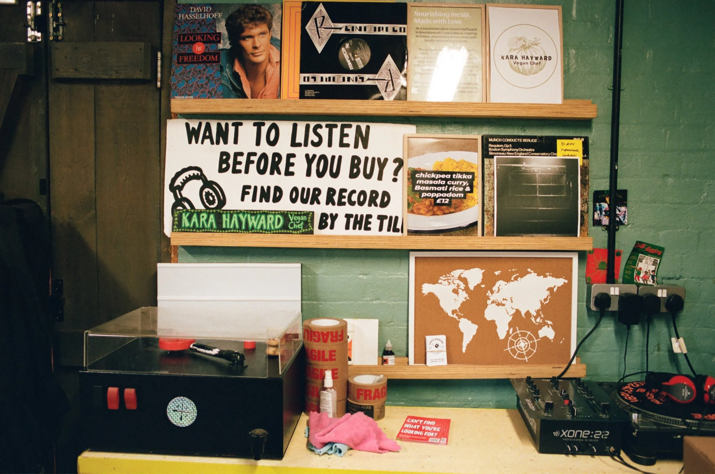 Record-shop display featuring vinyl records, a turntable, framed artwork and vegan food signage. Photo by Shahab Notghi.