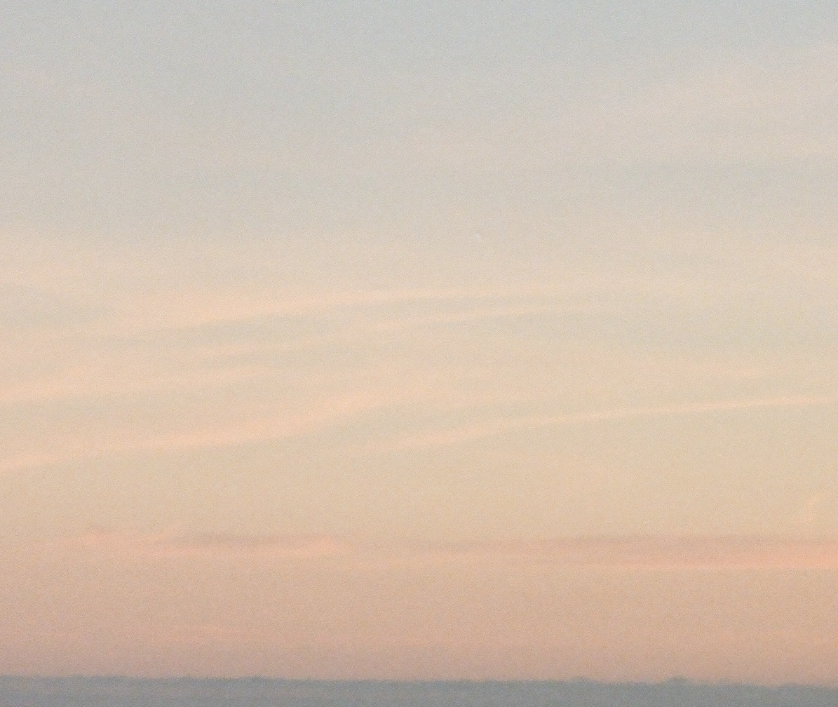 Calm sky at sunset with soft pink and orange clouds over a distant horizon.