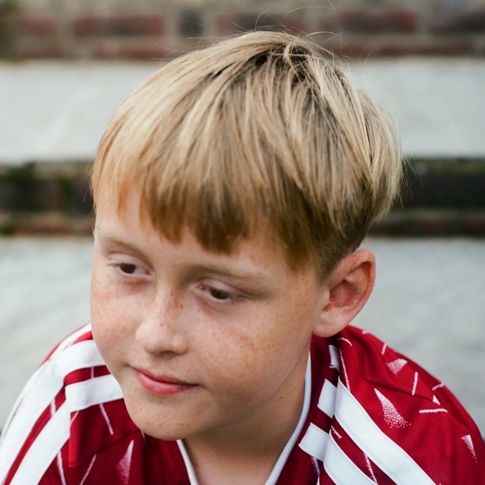 Close-up of a child's face with red hair, freckled skin, and wearing a red and white striped sports jersey.