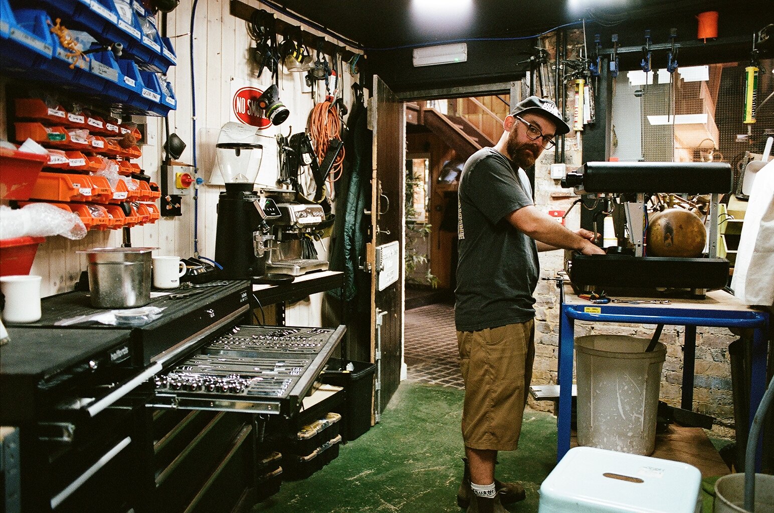 Technician working on a commercial coffee machine in a workshop filled with tools and equipment. Photo by Shahab Notghi.