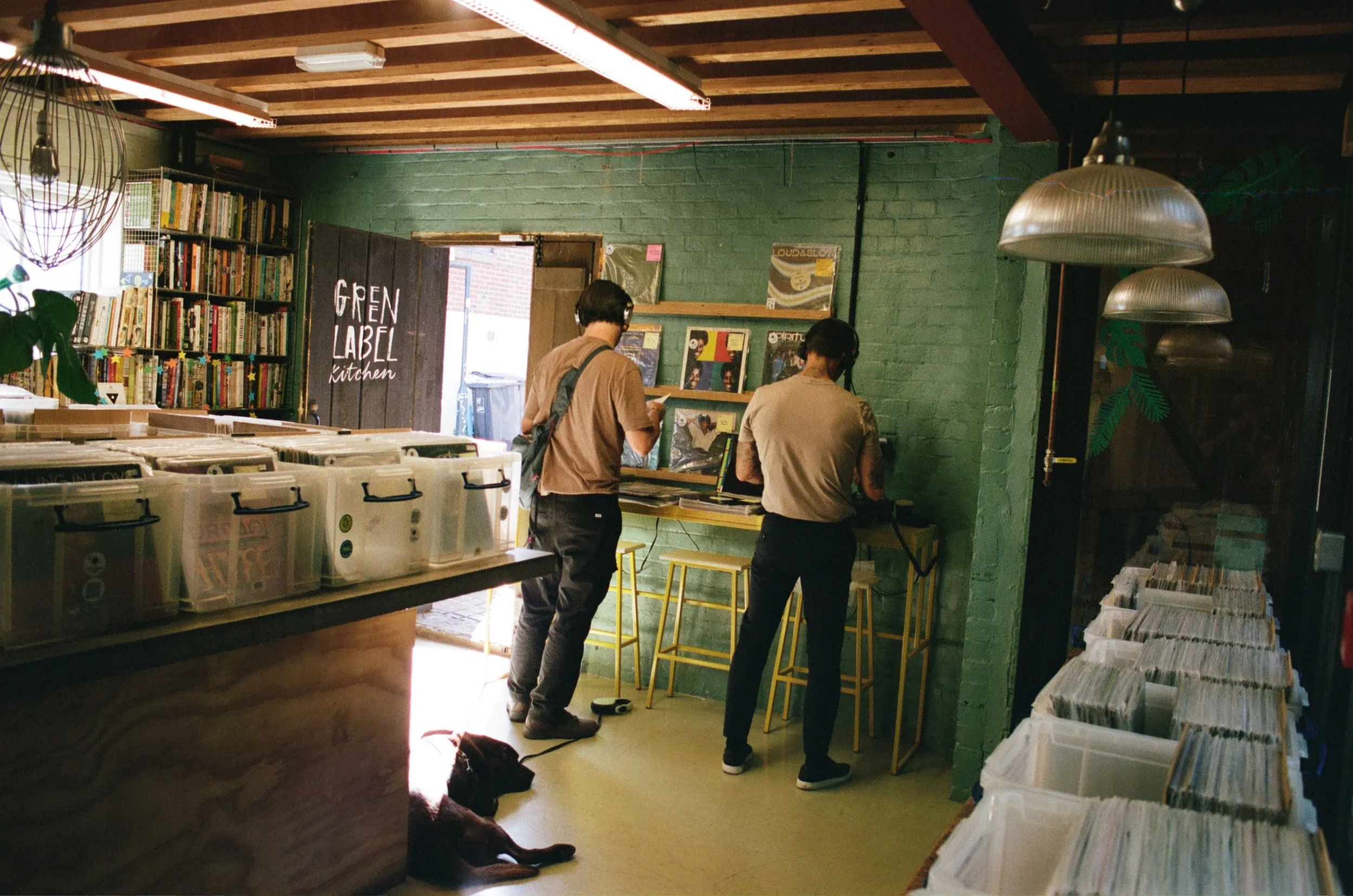 Two people browsing vinyl records inside a shop with record bins, shelves and pendant lights. Photo by Shahab Notghi.