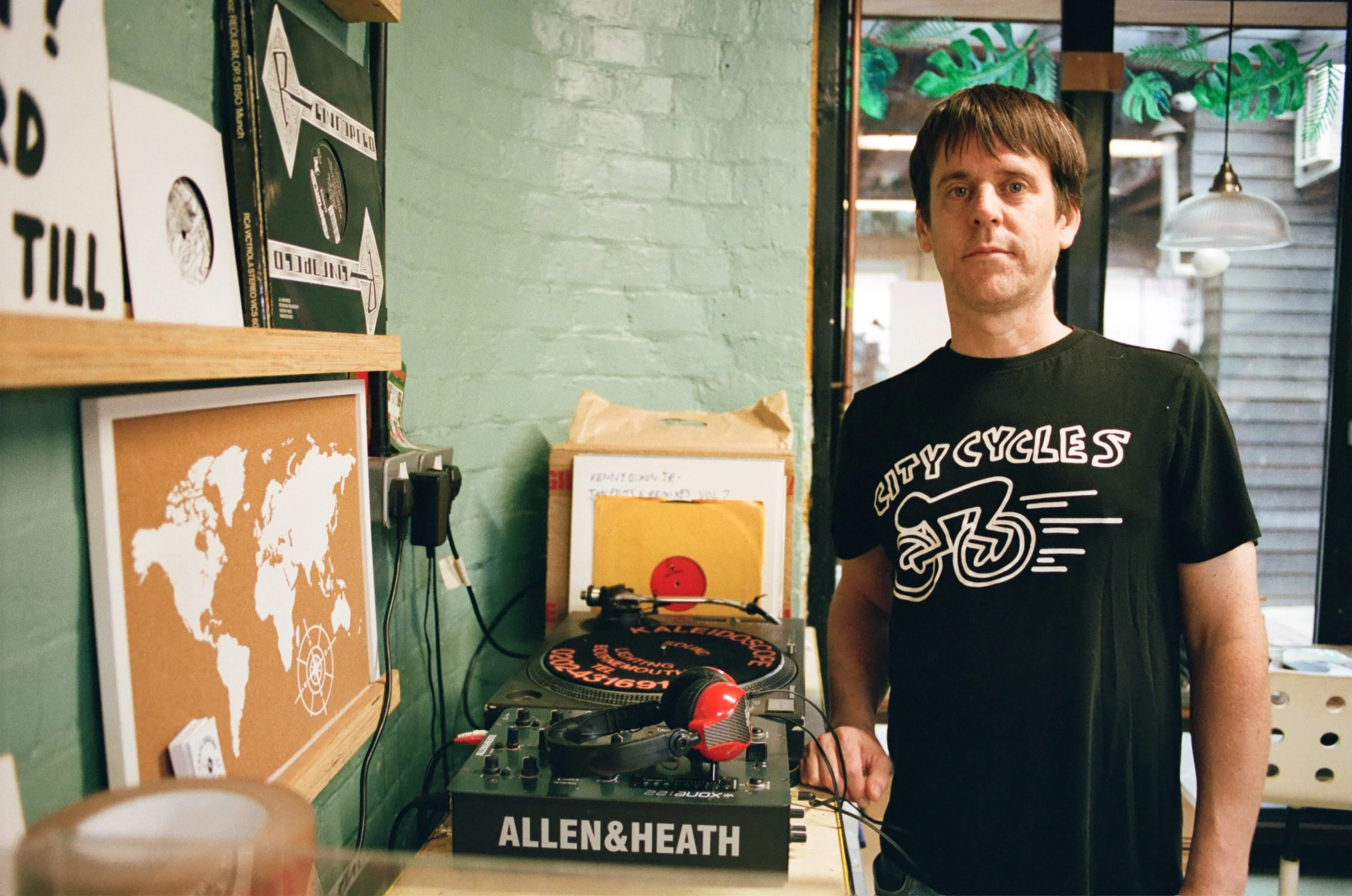 Portrait of a man standing beside a turntable and vinyl records in a record shop. Photo by Shahab Notghi.