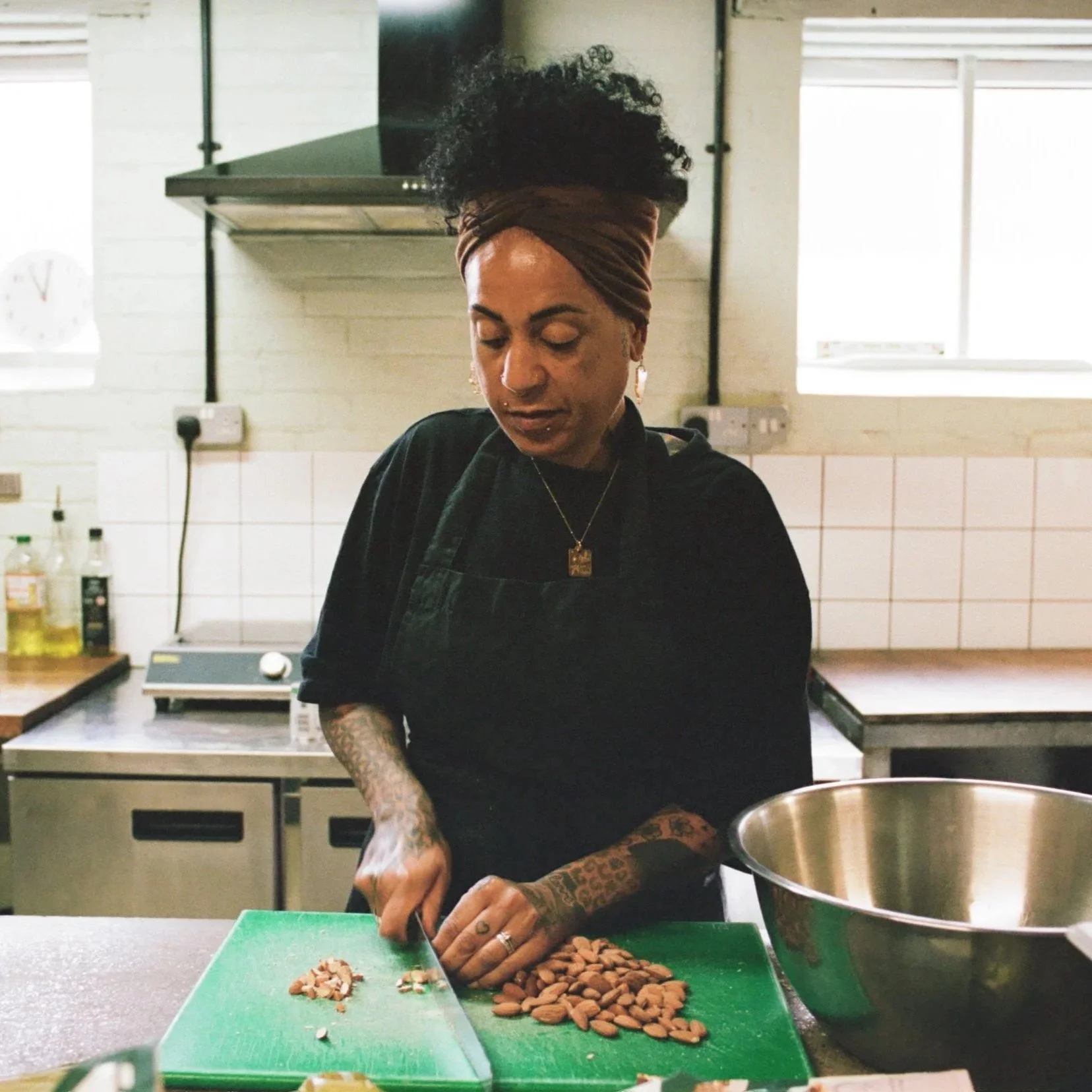 Vegan chef chopping almonds on a green cutting board in a professional kitchen. Photo by Shahab Notghi.