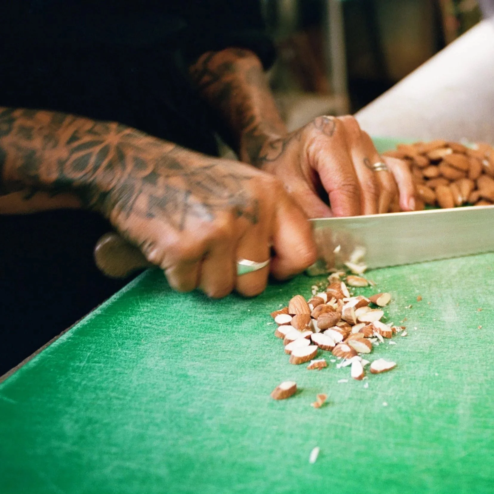 Close-up of a chef's hands chopping almonds on a green cutting board. Photo by Shahab Notghi.