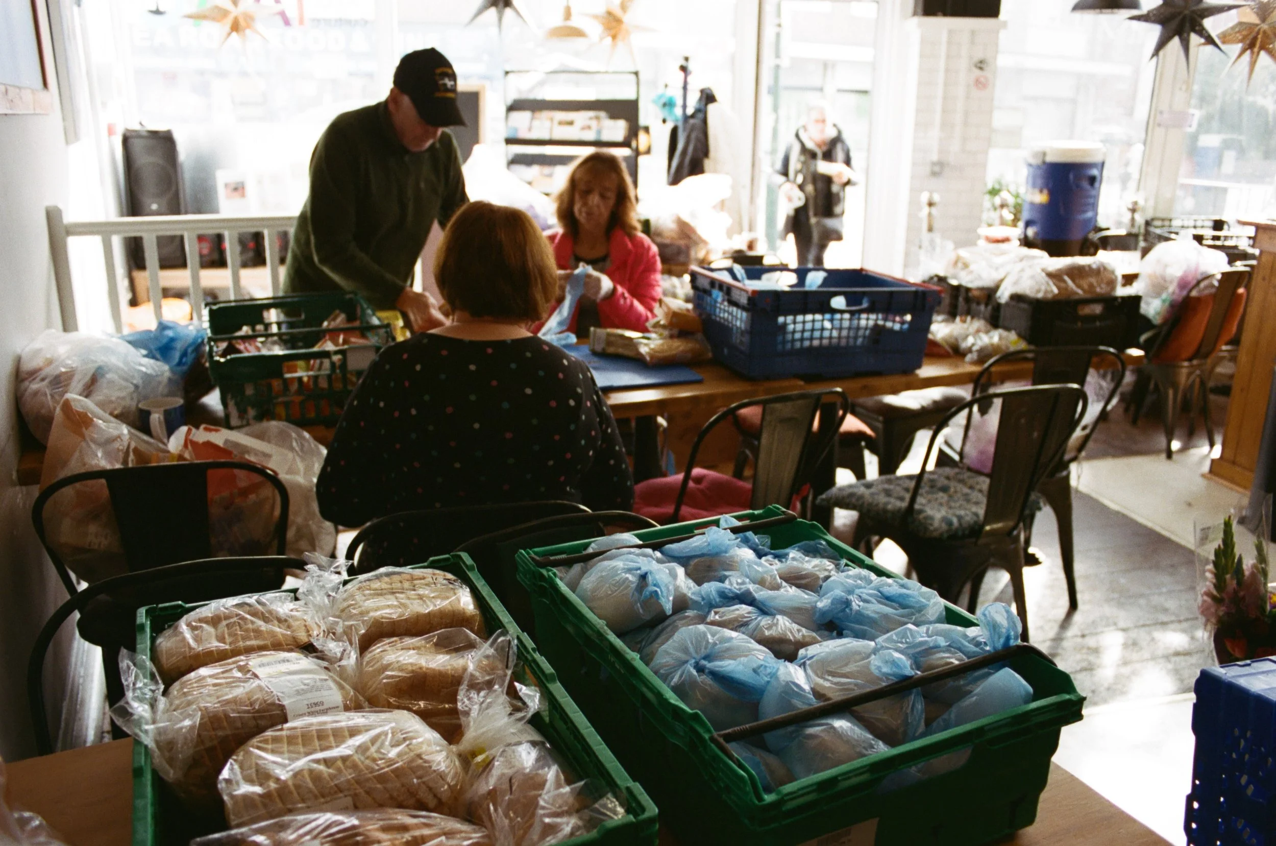 People at a market or food drive organizing and sorting bread and groceries on tables.