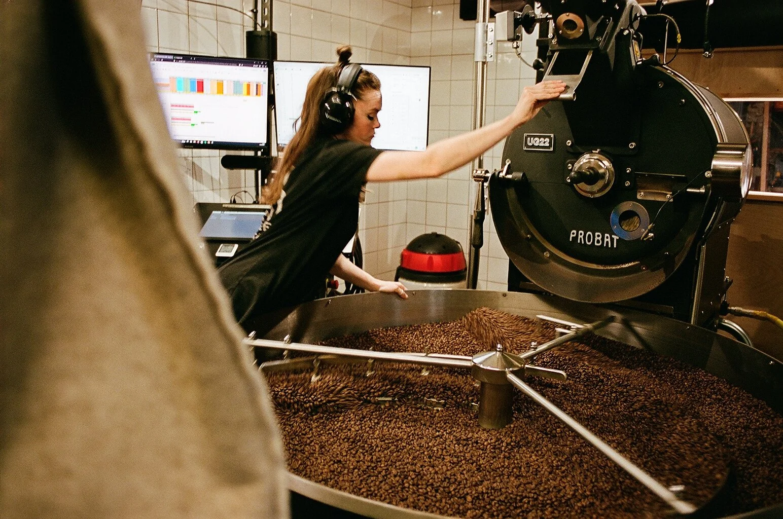 Roastery worker monitoring coffee beans inside a Probat commercial coffee roasting machine. Photo by Shahab Notghi.