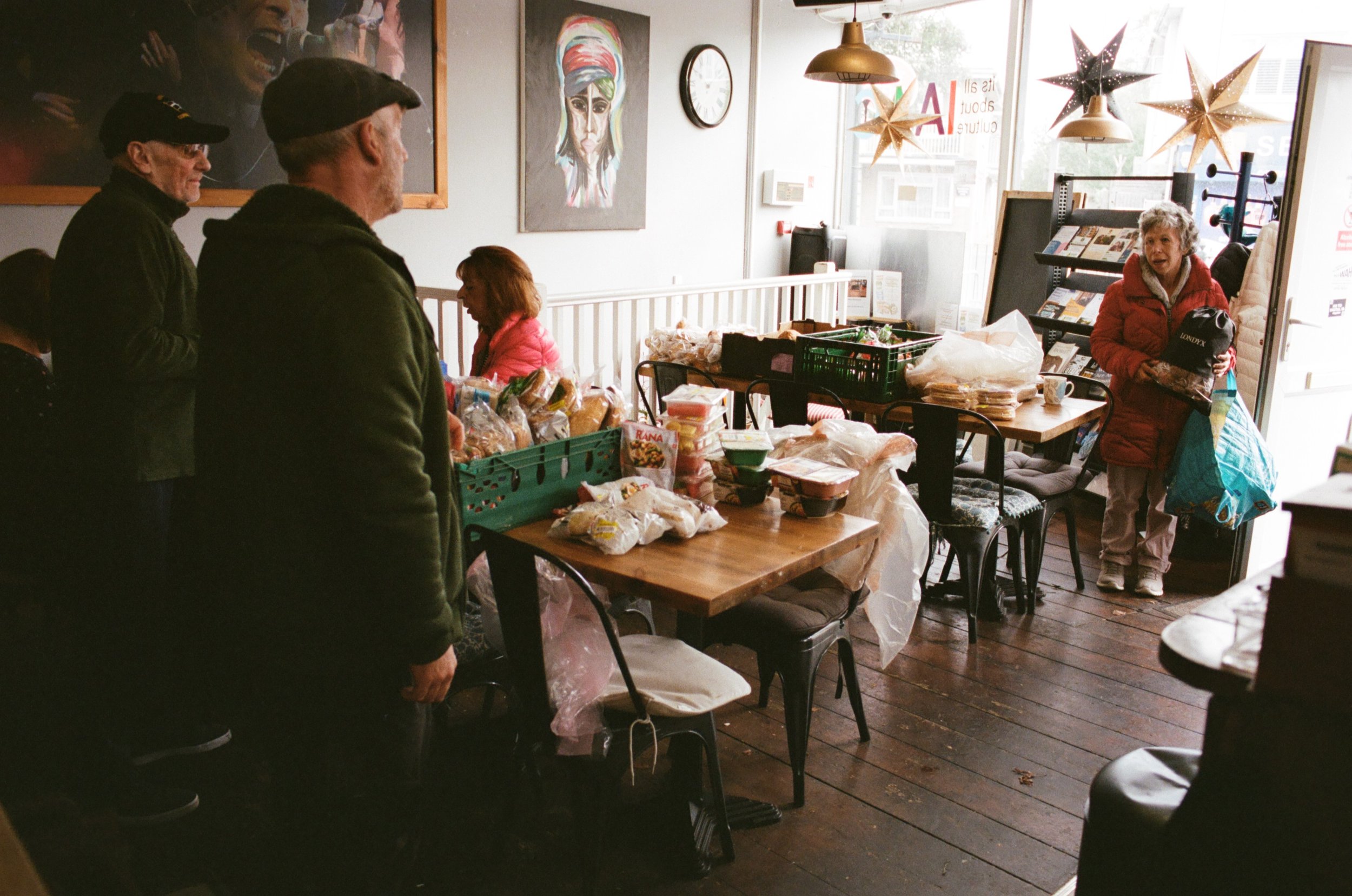 People shopping at a grocery store or food drive, with animated artwork on the wall and holiday star decorations hanging from the ceiling.