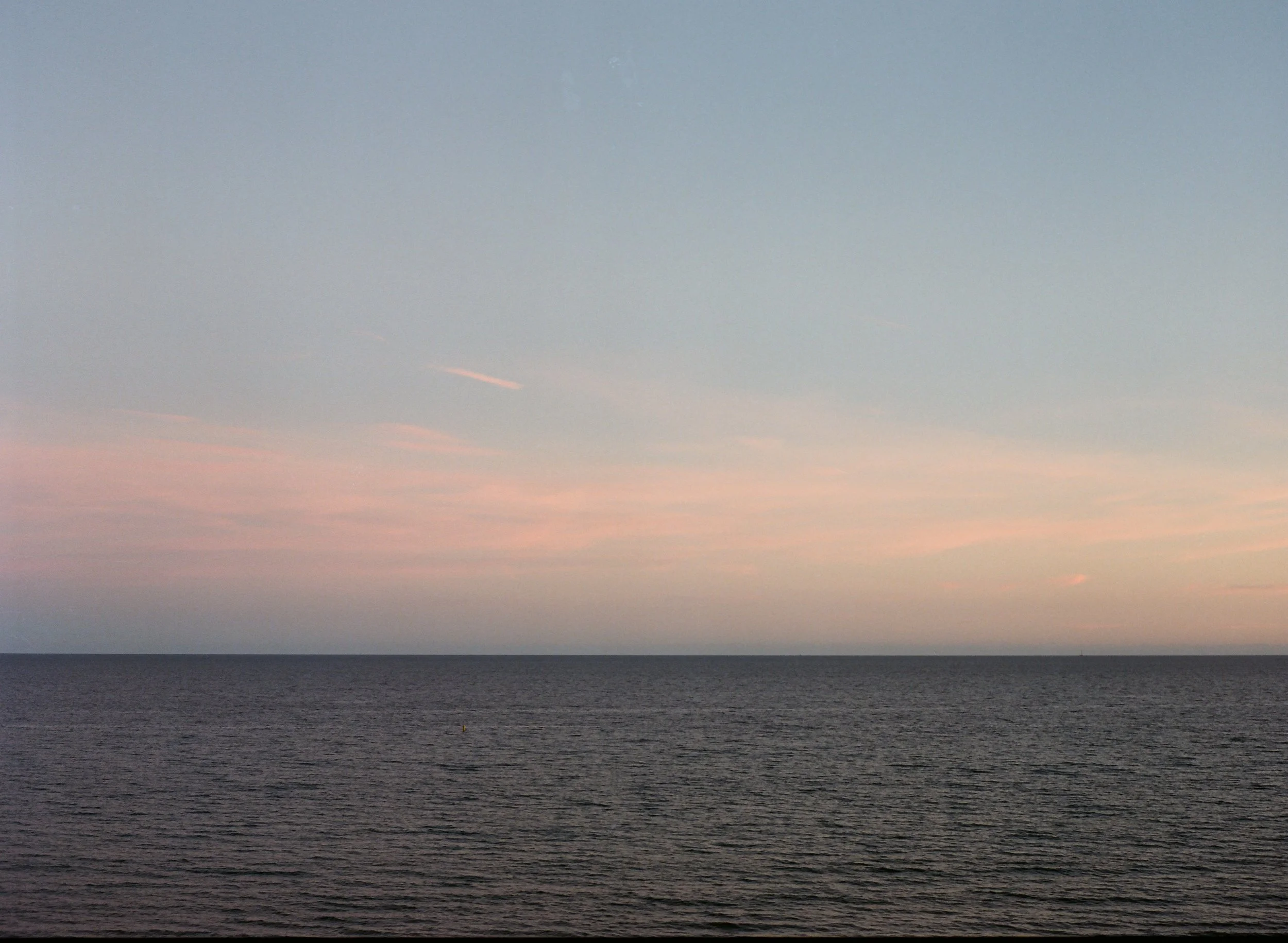 A panoramic view of the ocean at sunset with a pastel-colored sky and a calm sea.