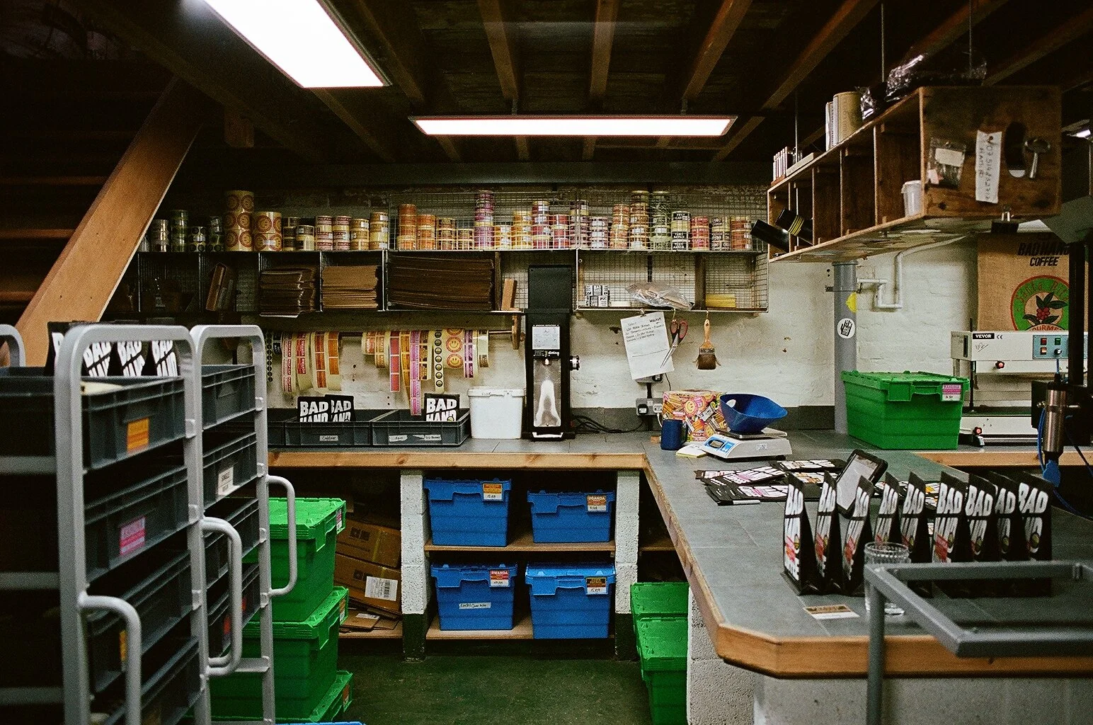 Interior view of Bad Hand Coffee's roastery, showing workbenches, branded coffee bags, storage crates and equipment. Photo by Shahab Notghi.