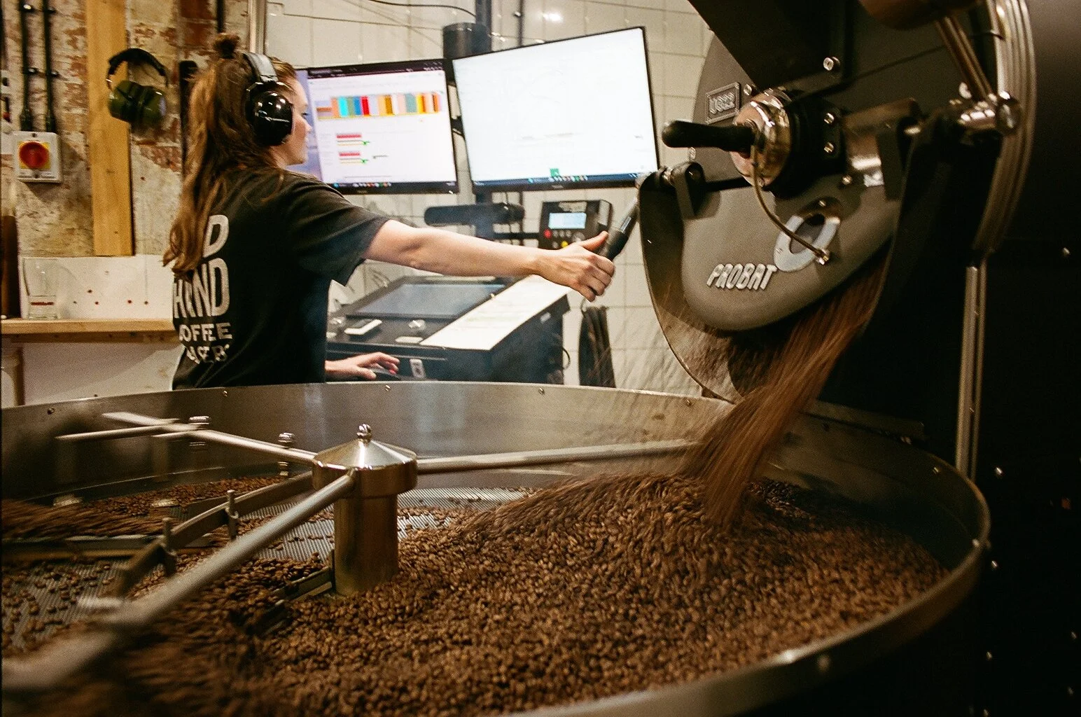 Coffee roaster operating a large industrial machine as freshly roasted coffee beans tumble inside. Photo by Shahab Notghi.