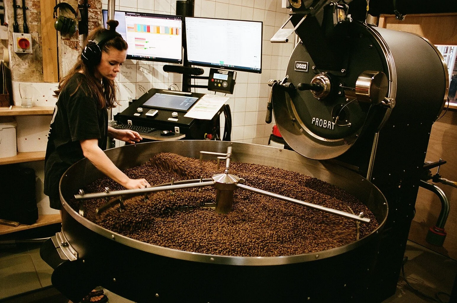 Roastery worker checking freshly roasted coffee beans in the cooling tray of an industrial roaster. Photo by Shahab Notghi.