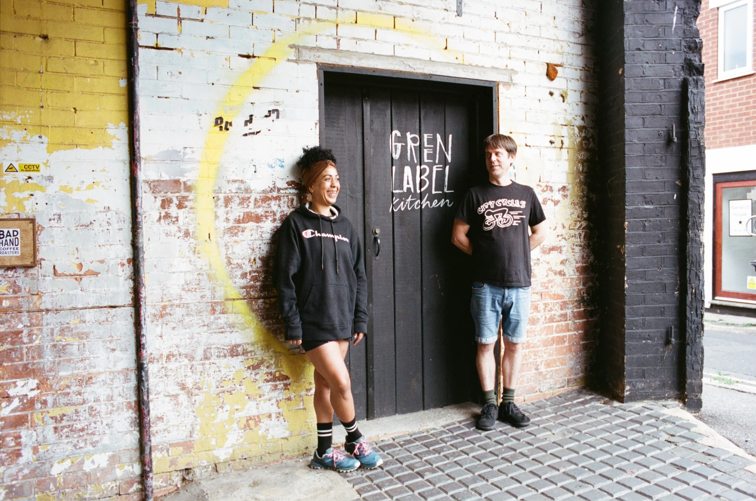 Two Green Label Kitchen team members standing outside the kitchen entrance in Bournemouth. Photo by Shahab Notghi.