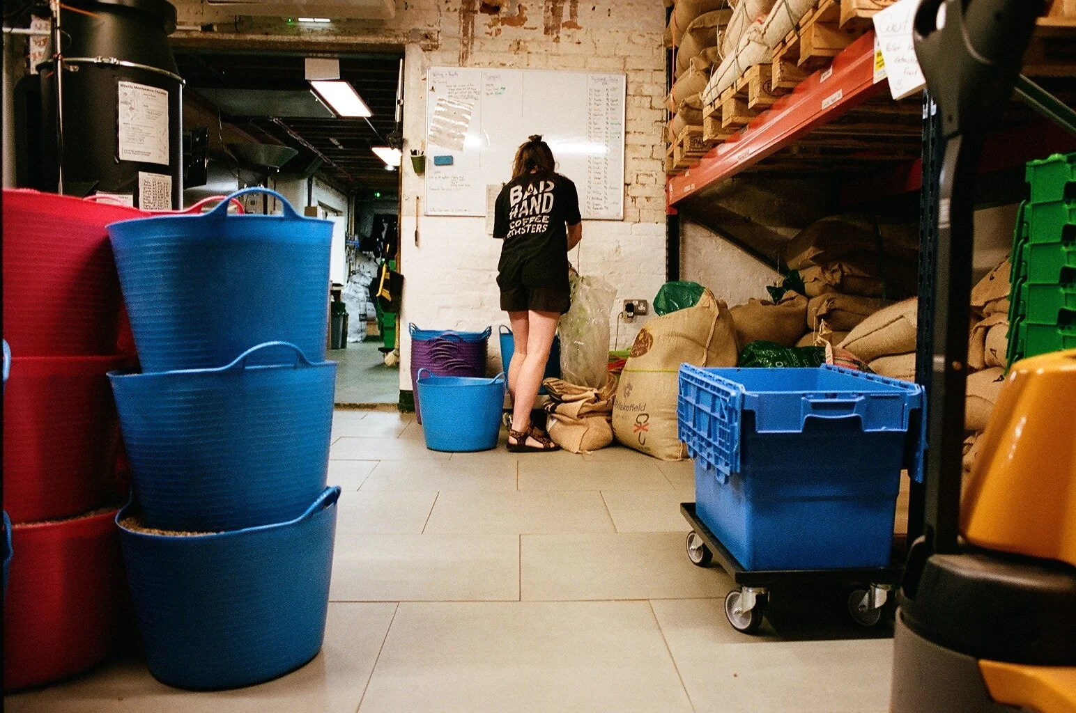 Coffee roastery workspace with industrial roasting machinery, stacked coffee sacks and colourful storage crates. Photo by Shahab Notghi.