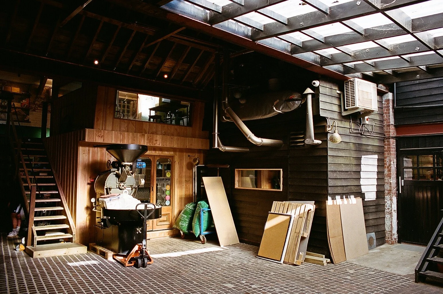Industrial interior of Bad Hand Coffee's Bournemouth roastery, featuring roasting equipment, brick walls and wooden workspaces. Photo by Shahab Notghi.